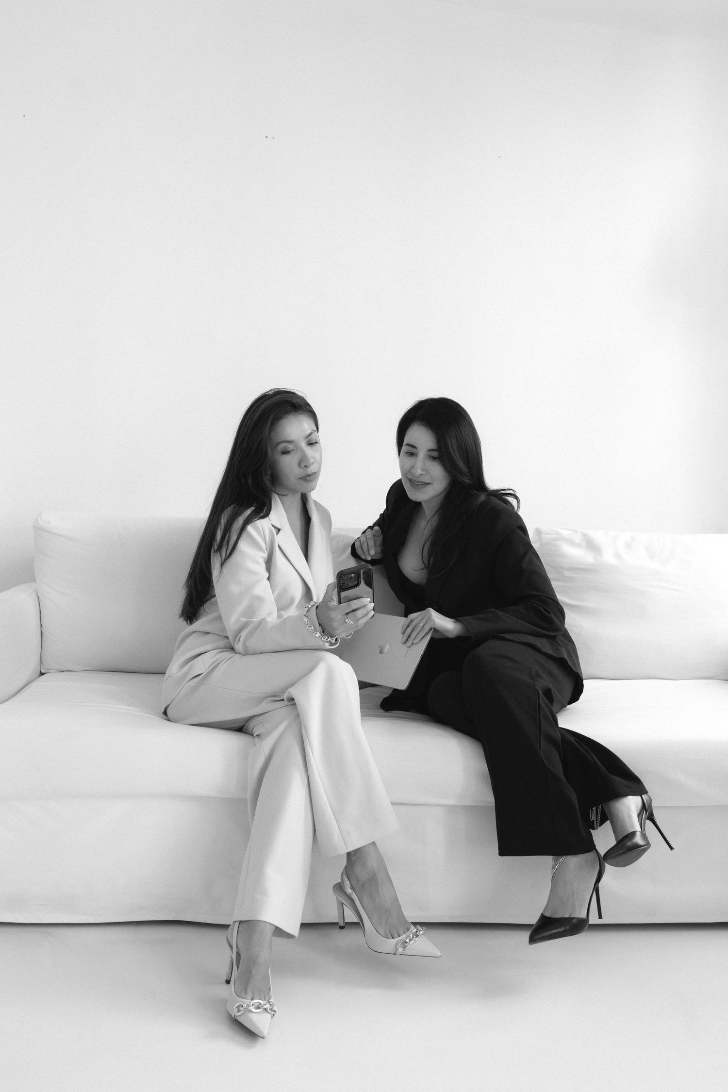 Two figures in contrasting black and white outfits seated on a white sofa in a minimalist style photoshoot sequence.