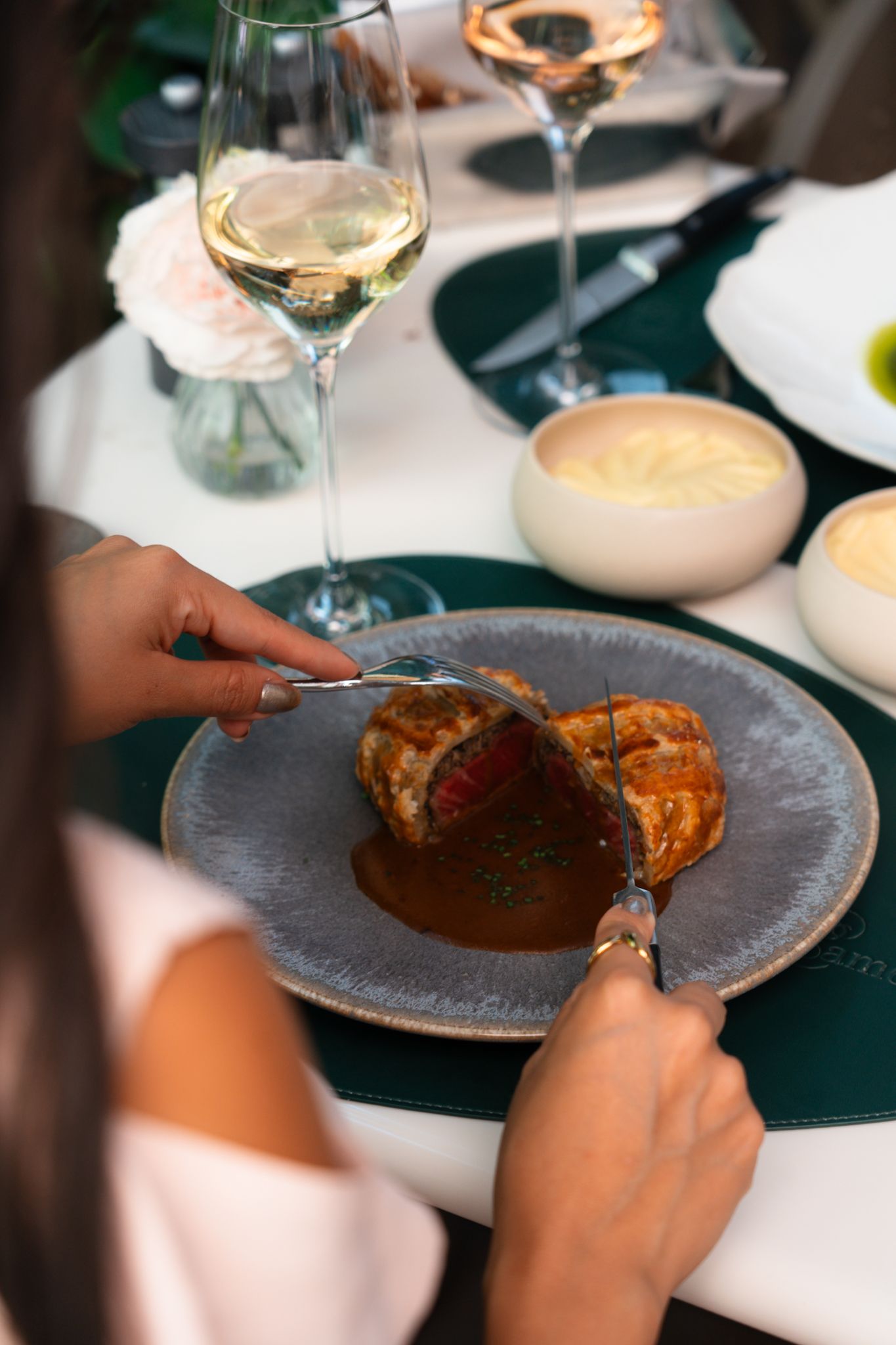 Person using fork and knife to cut into a gourmet plated meal served on a gray stoneware dish at an upscale restaurant.