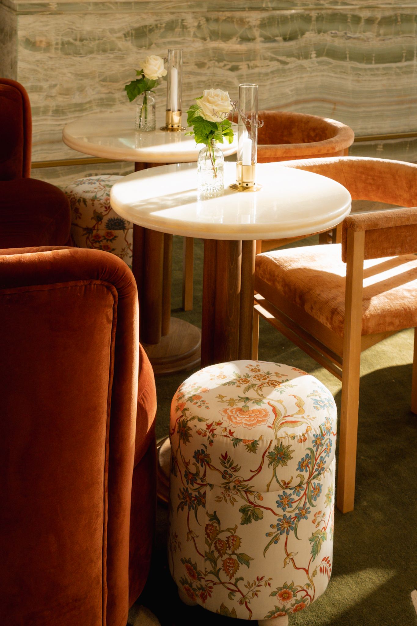 Elegant restaurant lounge with velvet chairs, marble tables, and floral ottoman in warm amber lighting.