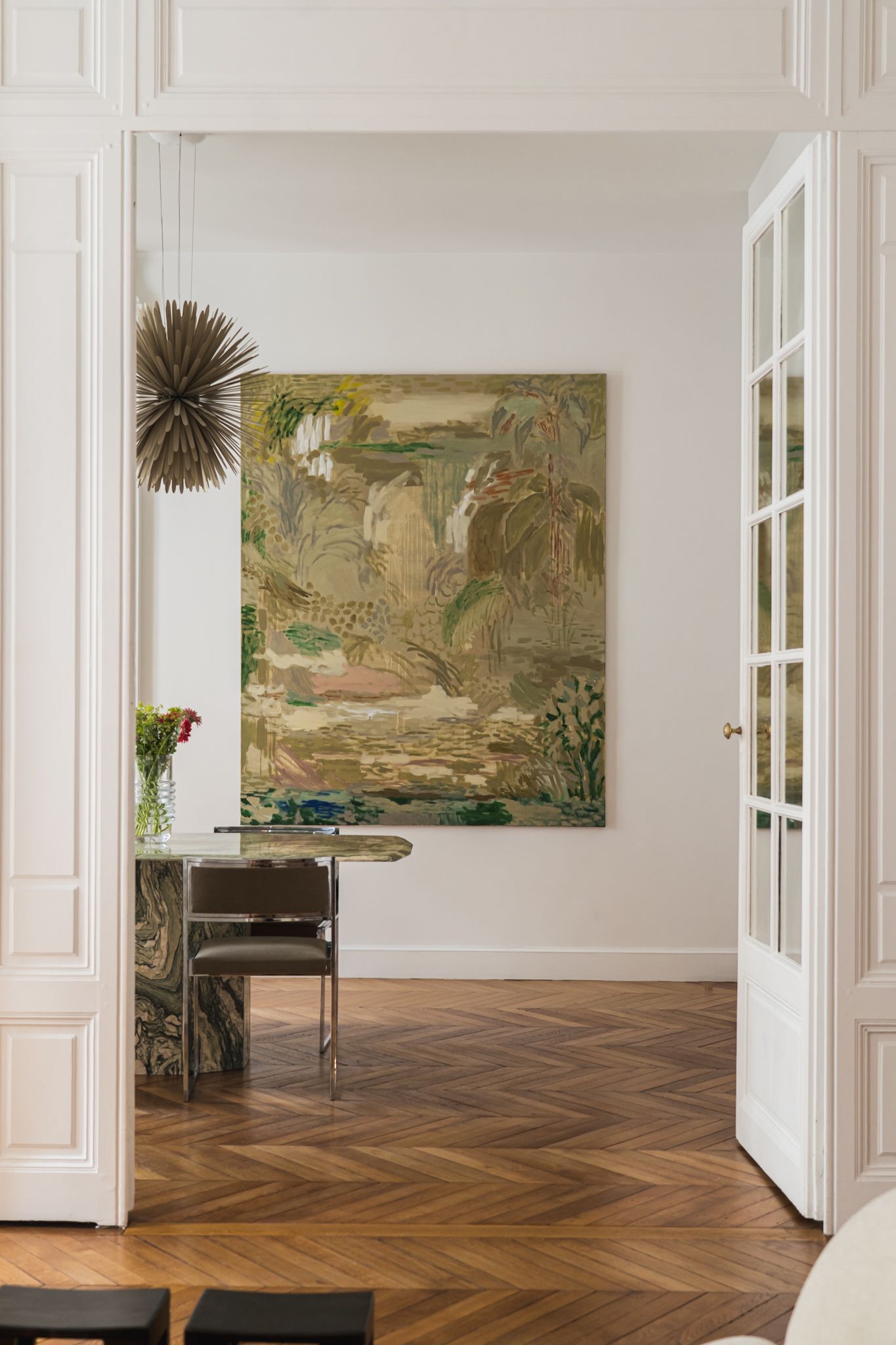 Elegant interior room with herringbone floors and large decorative botanical artwork on white walls.