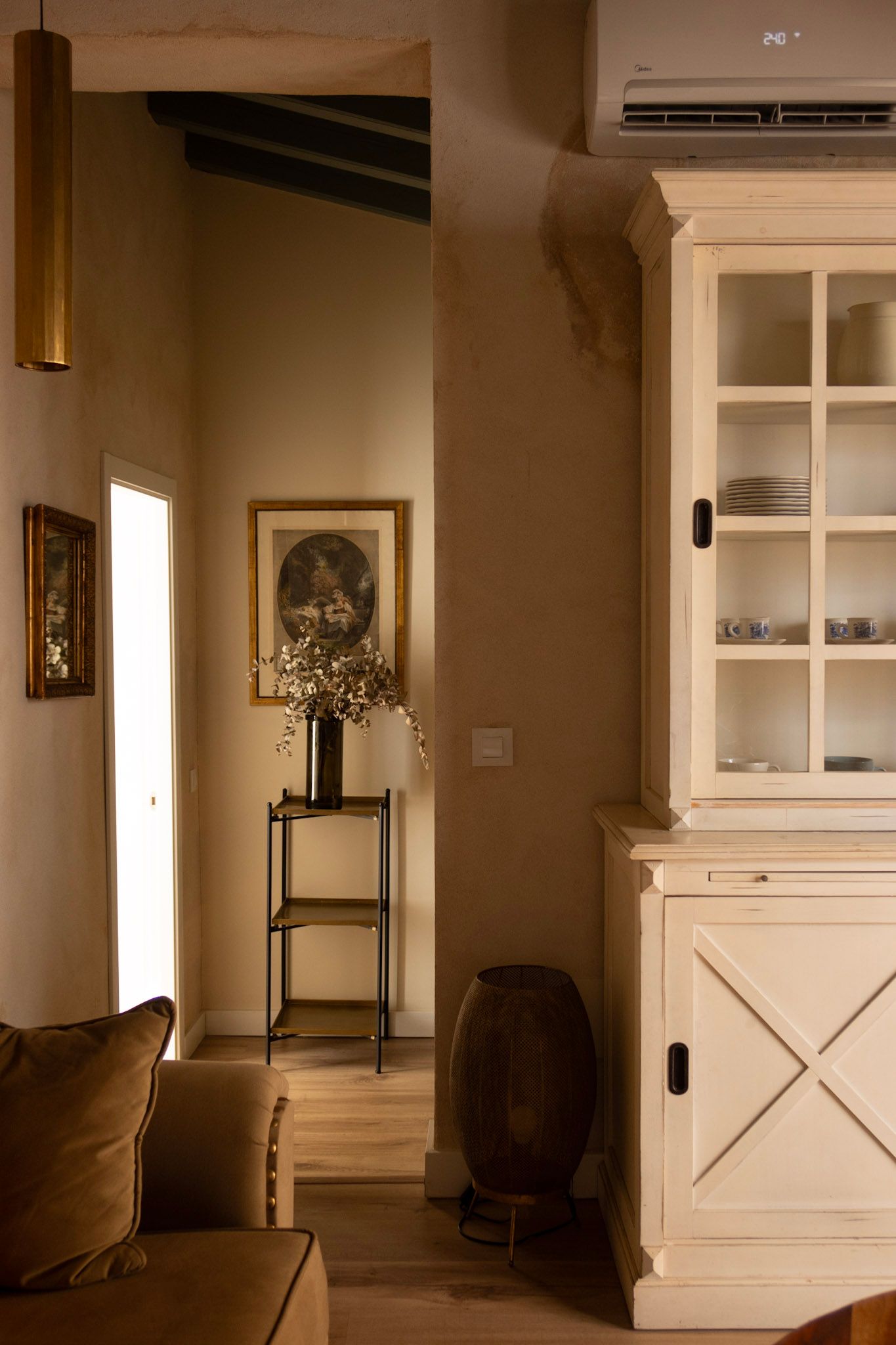 A cozy interior corner with a white cabinet, golden pendant light, wooden floors and vintage decor elements.