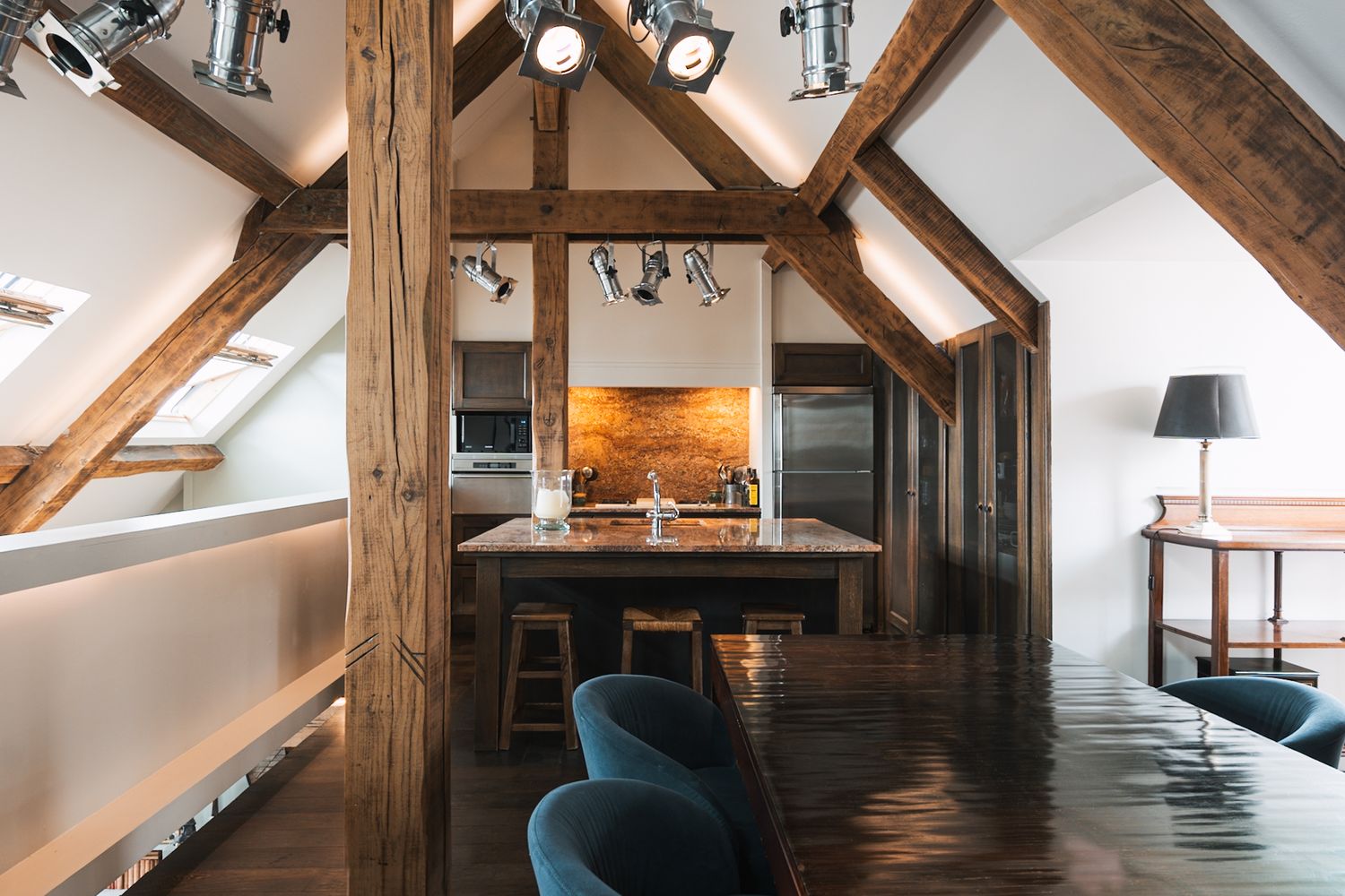 Luxurious attic apartment interior with exposed wooden beams, modern kitchen, and teal velvet accent chair.