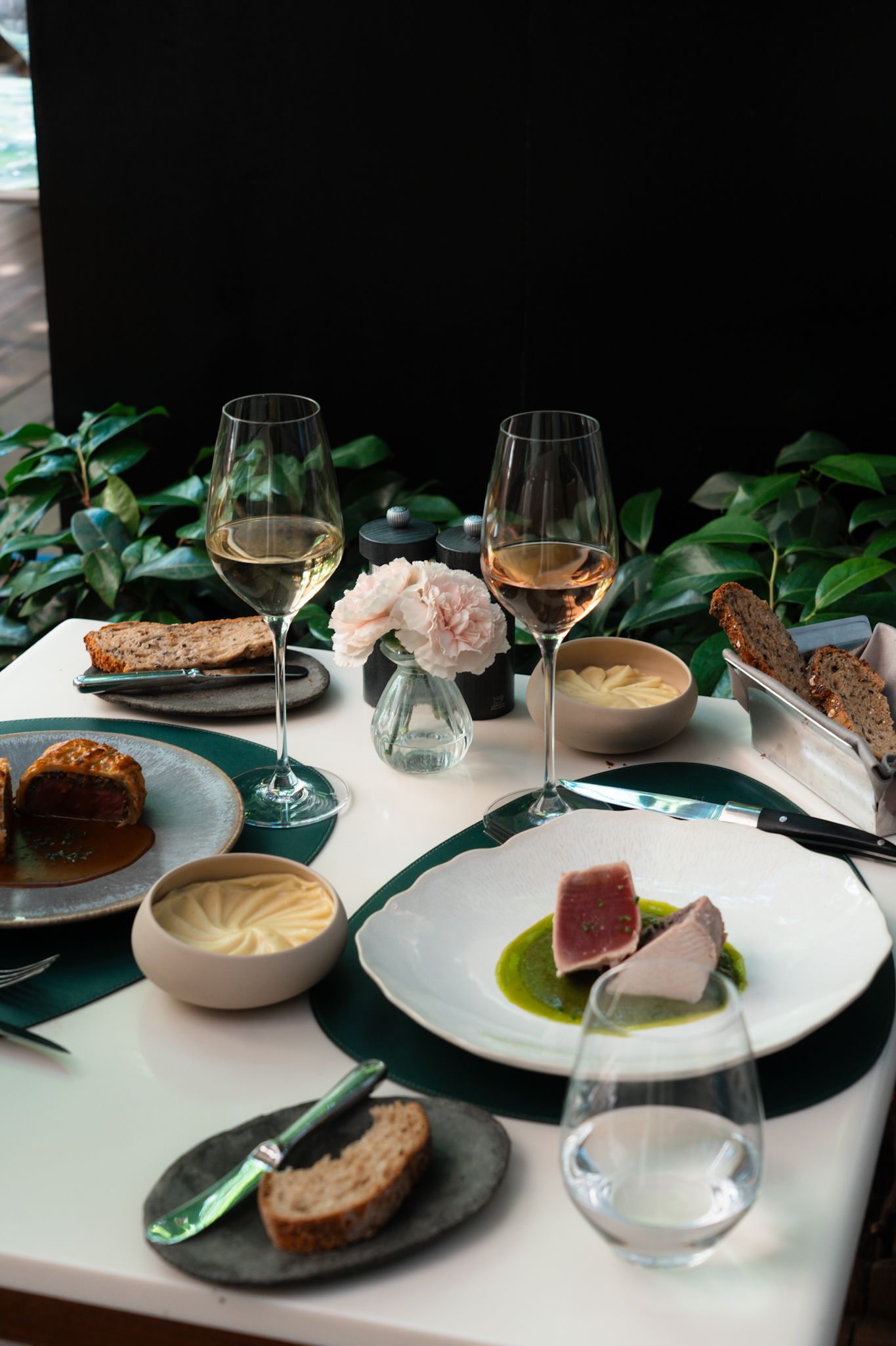 An elegant restaurant table setting featuring multiple dishes, wine glasses, and green foliage accents on white plates.