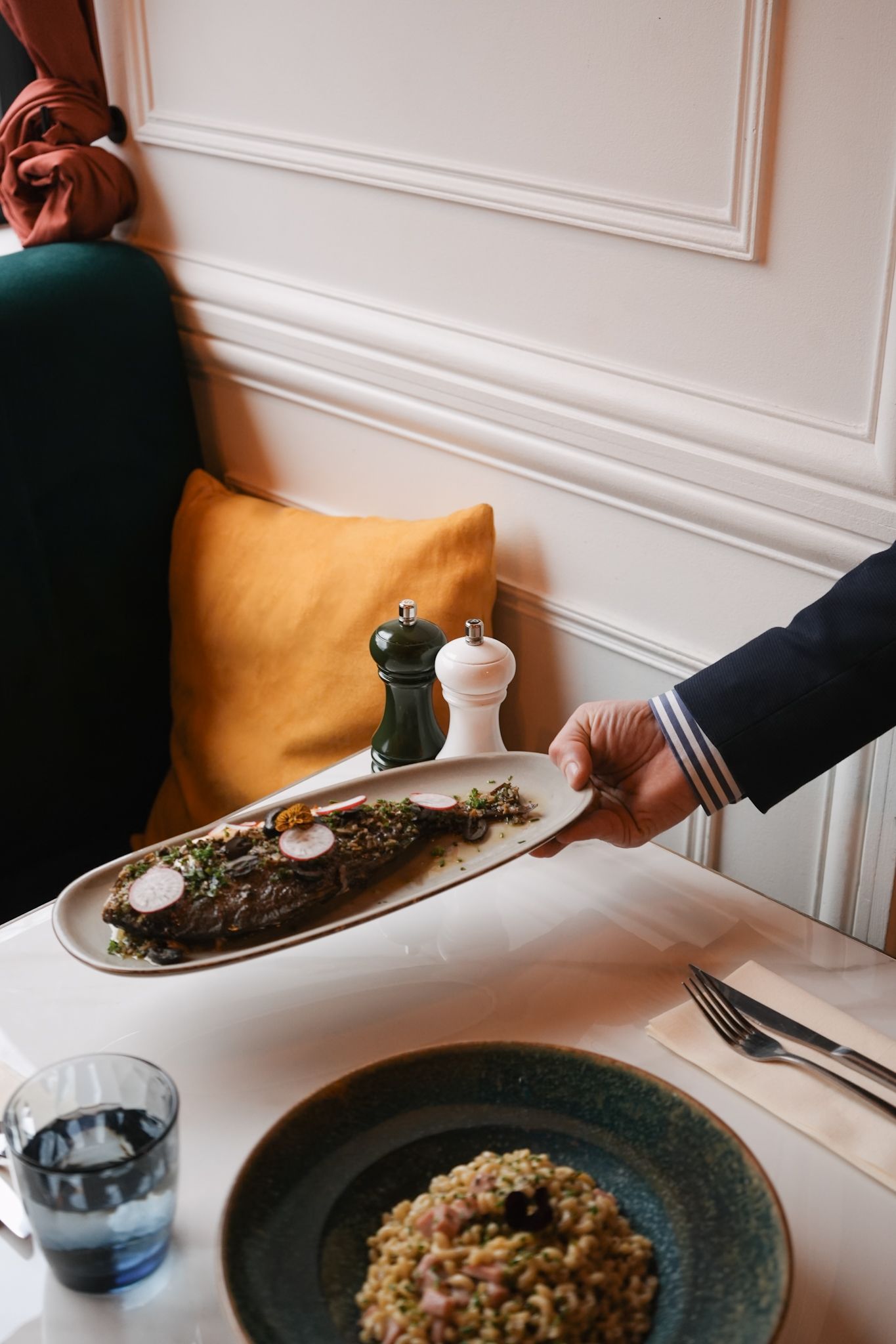 Elegantly plated fish dish alongside pearl couscous with herbs served on rustic blue plates in an upscale dining setting.