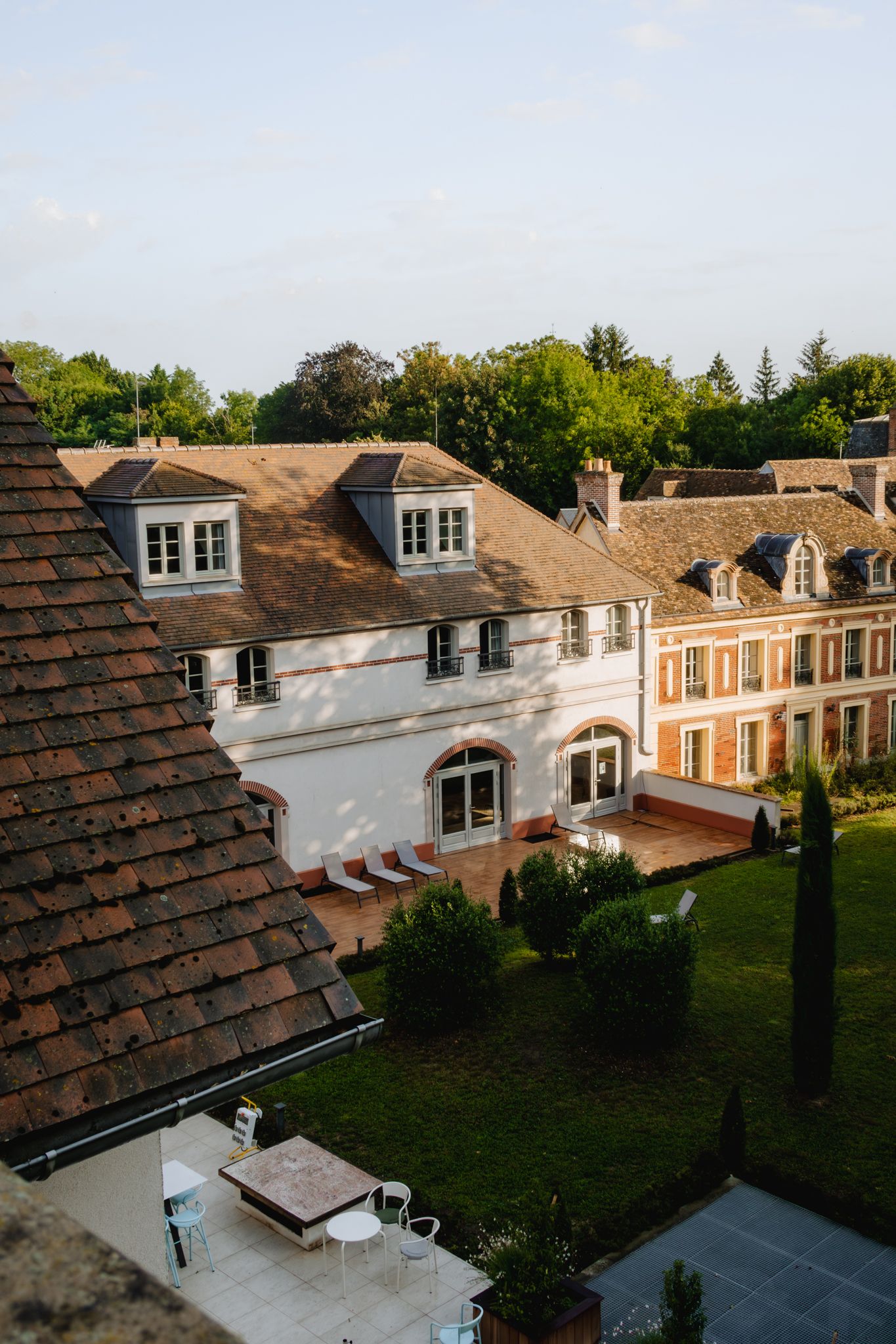 Elegant French country estate with terracotta roofs and dormer windows overlooks a manicured garden at sunset.