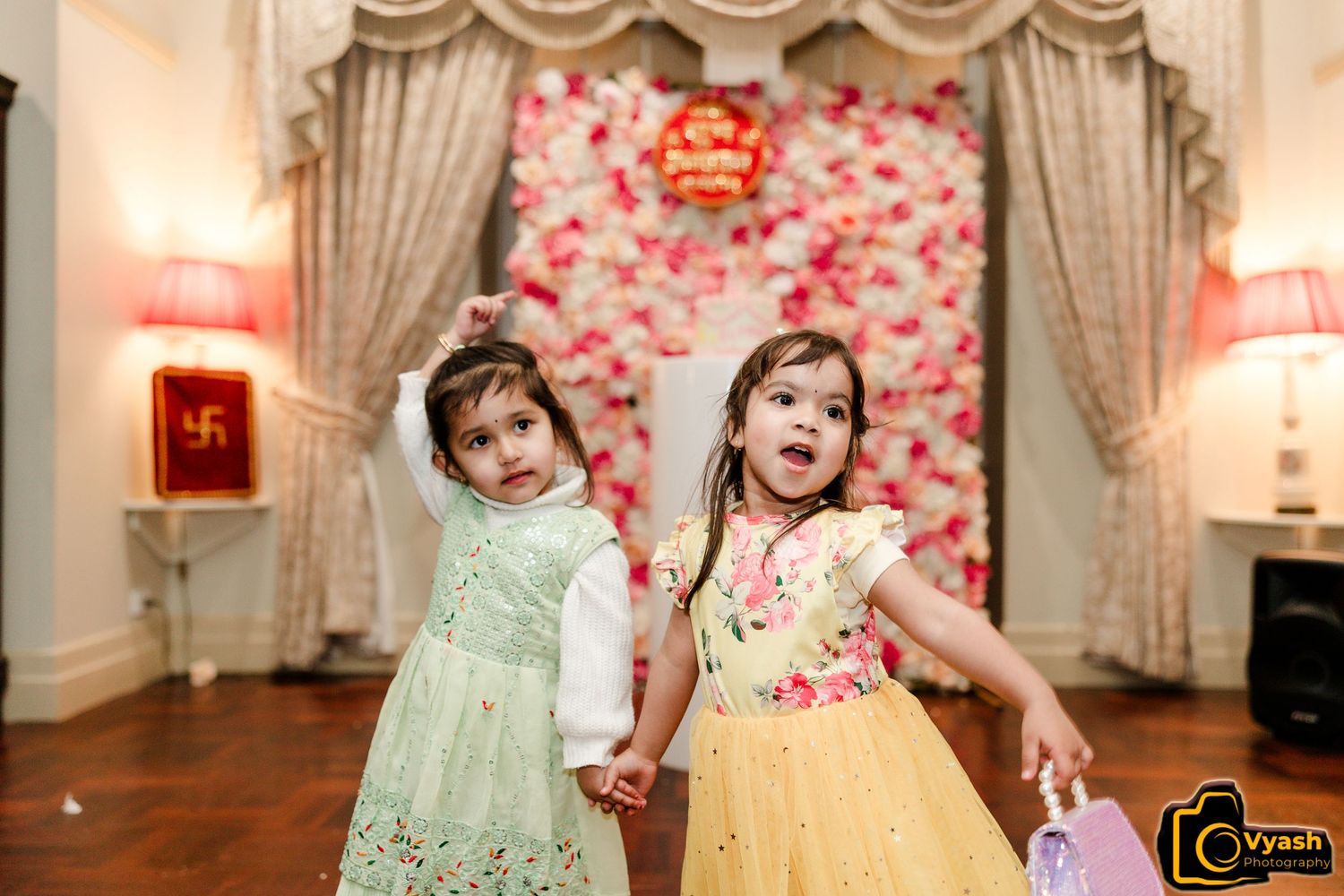 Two children in pastel dresses dancing and playing at an elegant party venue.