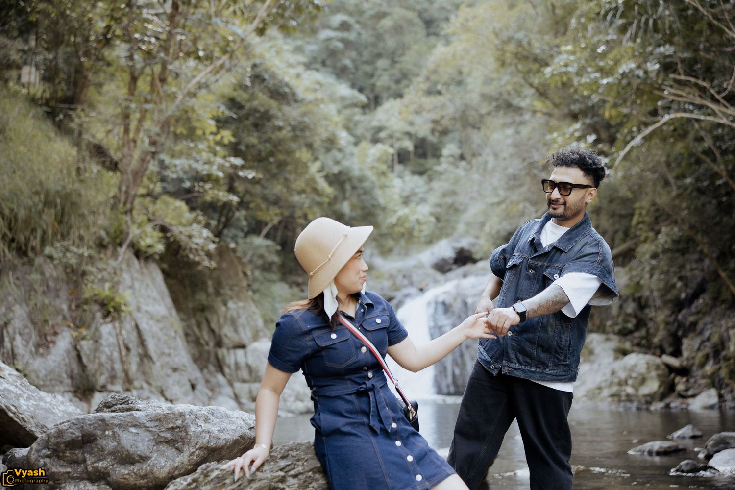 Couple in navy blue outfits playfully throwing autumn leaves in a romantic forest photoshoot along a river.
