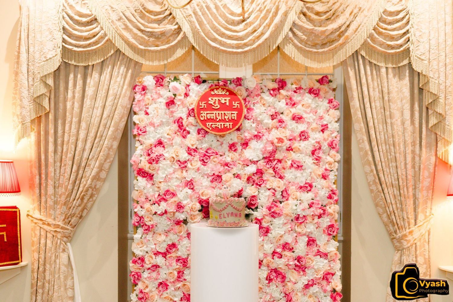 Elegant event backdrop with pink roses and cream drapes creating a romantic atmosphere.