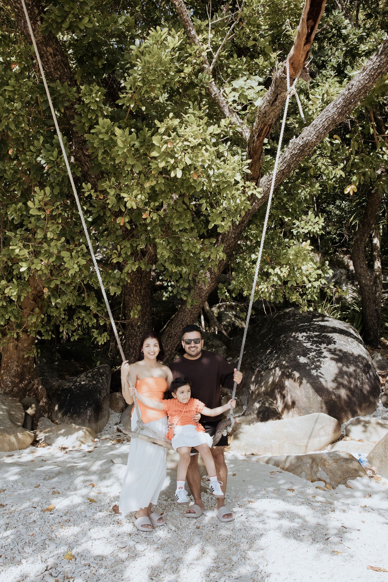 Two people sitting on rope swings in a shaded outdoor setting.