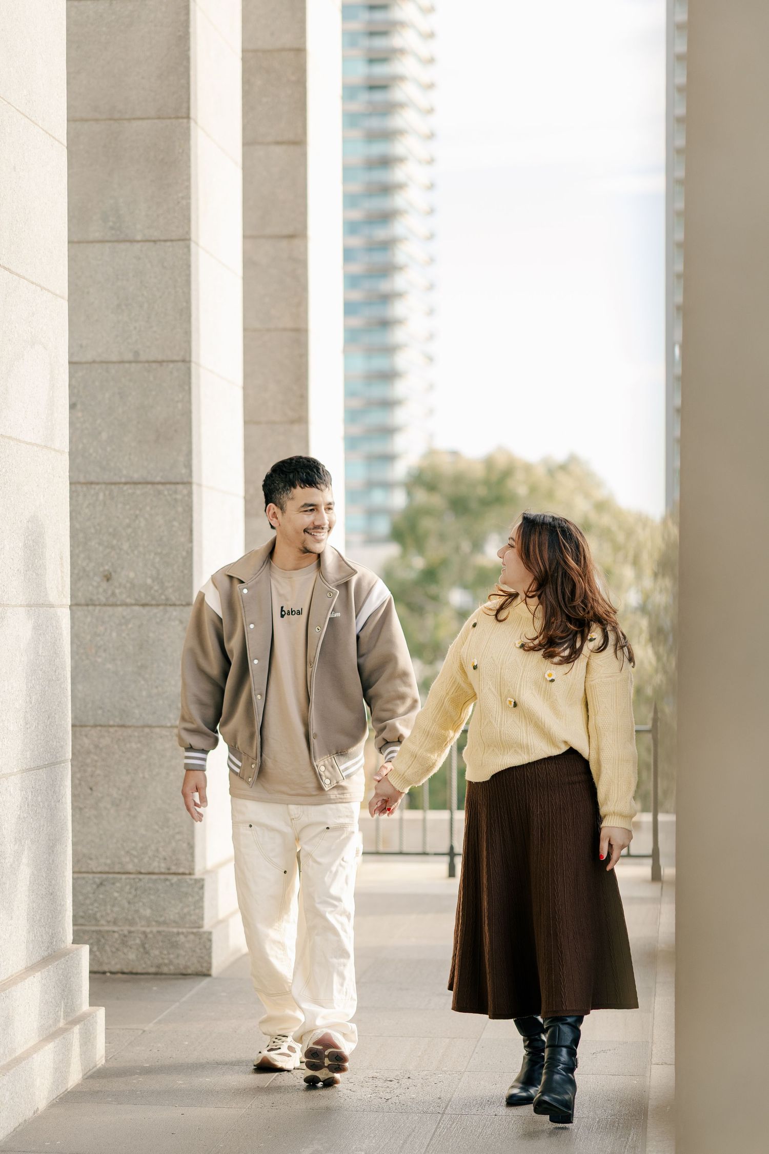 Couple dancing playfully between elegant stone pillars with city views.