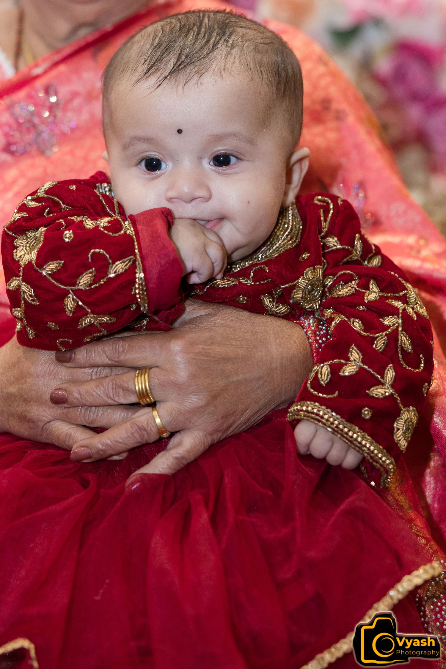 Baby wearing traditional red and gold embroidered outfit.