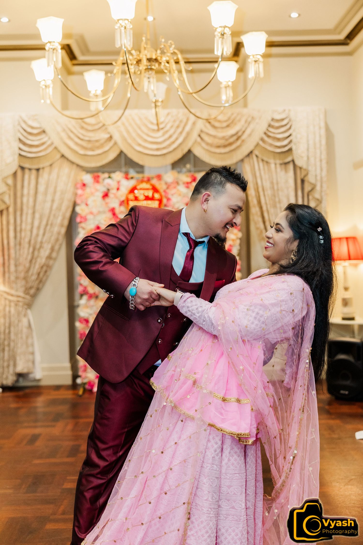A couple shares a romantic dance moment in formal attire under an elegant chandelier.