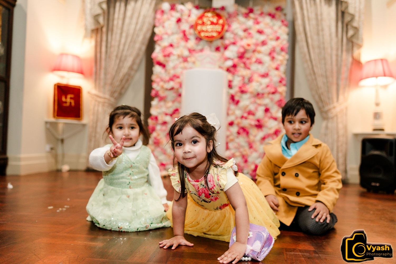 Children playing on the floor in front of a pink floral backdrop.