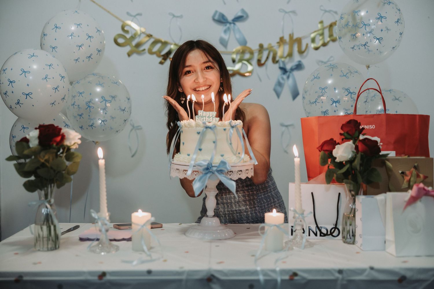 A birthday celebration setup with cake, candles, and balloons in blue and white theme.