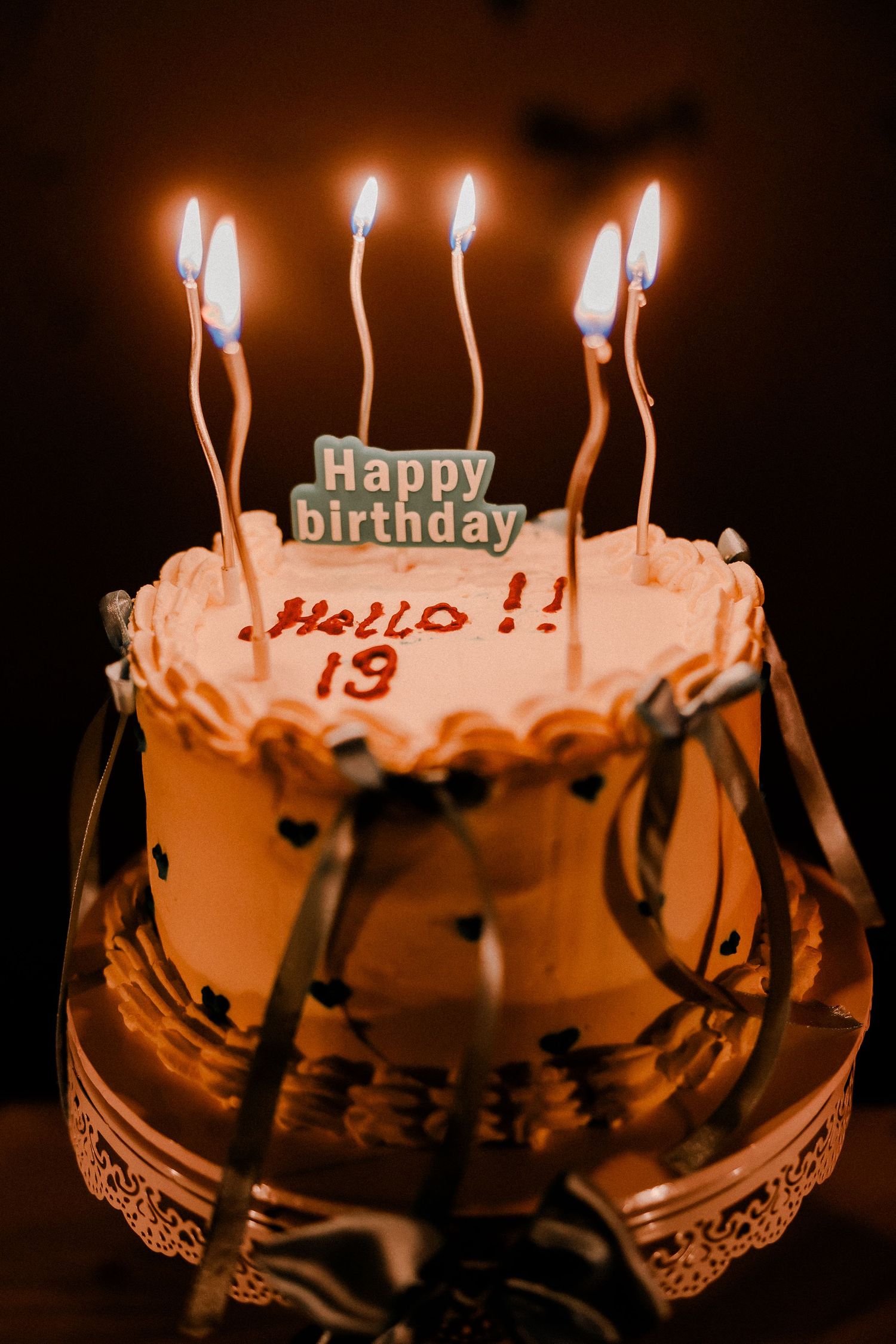 A birthday cake with lit candles reading 'Hello 19' in warm lighting.