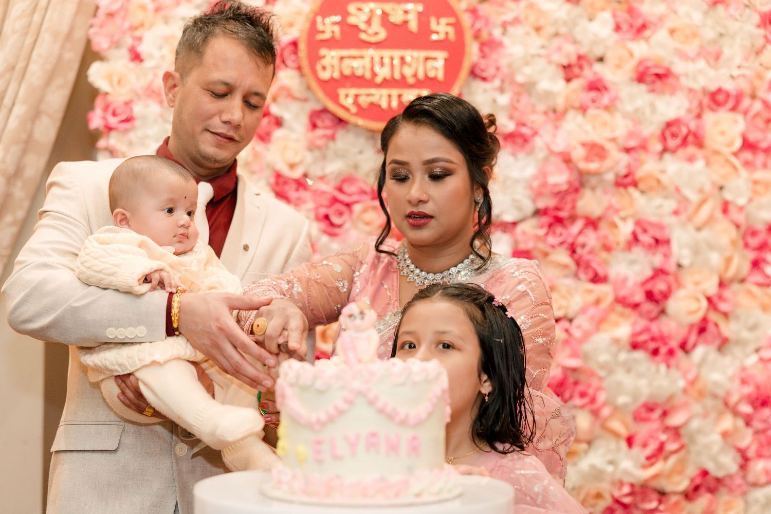 A family celebration moment with cake cutting against a pink floral backdrop.