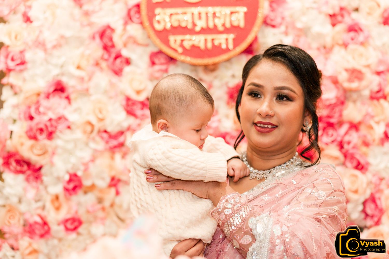 A cultural celebration moment captured against a pink floral wall with Nepalese text.