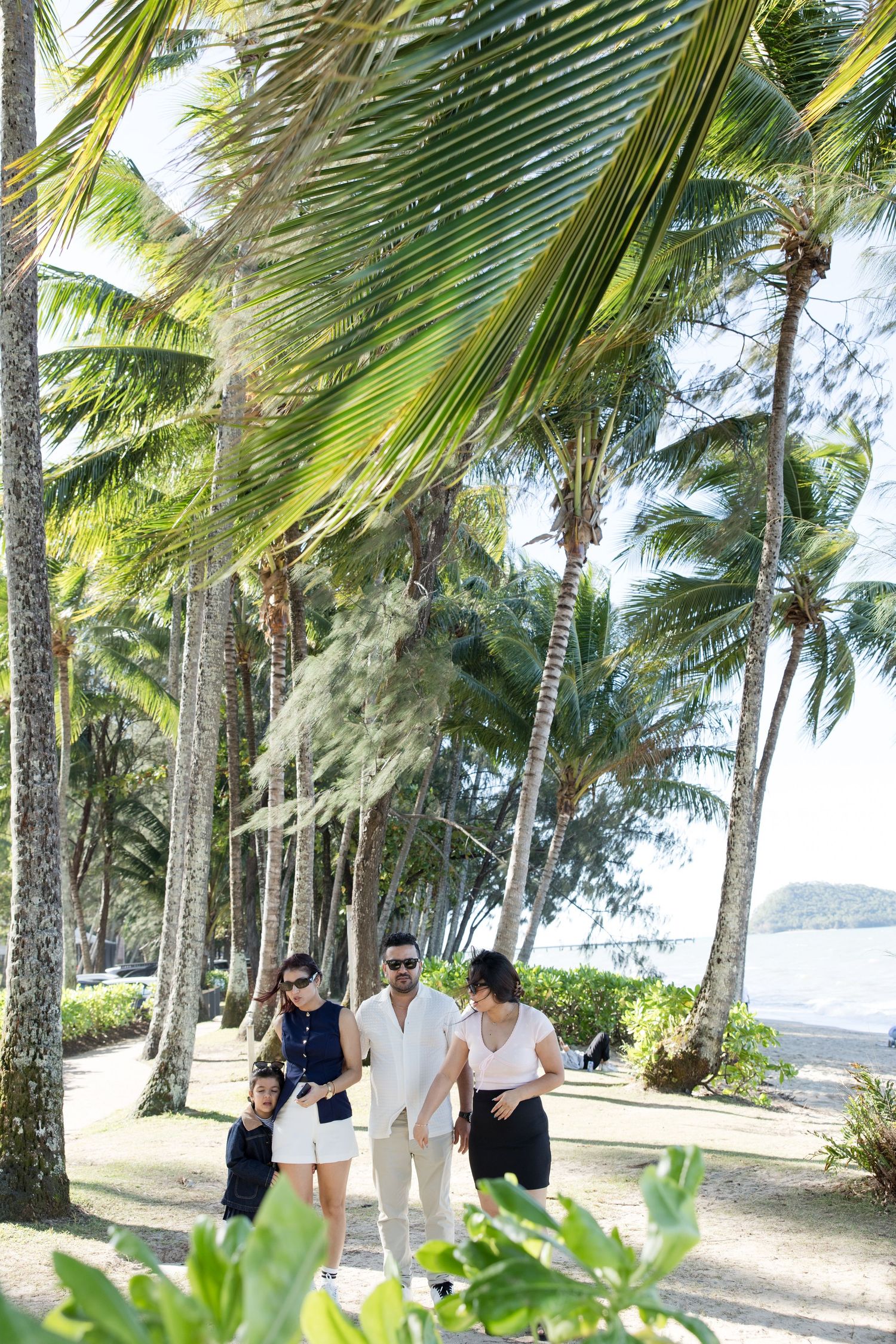 Family walking along a palm-lined coastal path on a sunny tropical day.