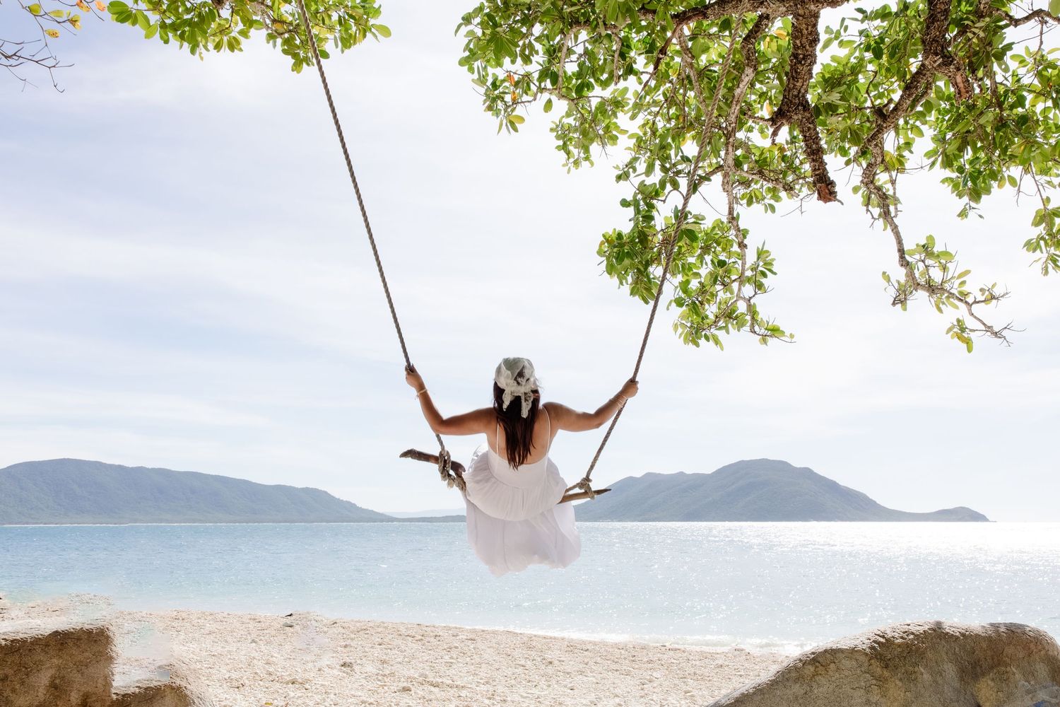 Person on swing overlooking scenic mountain and ocean landscape.
