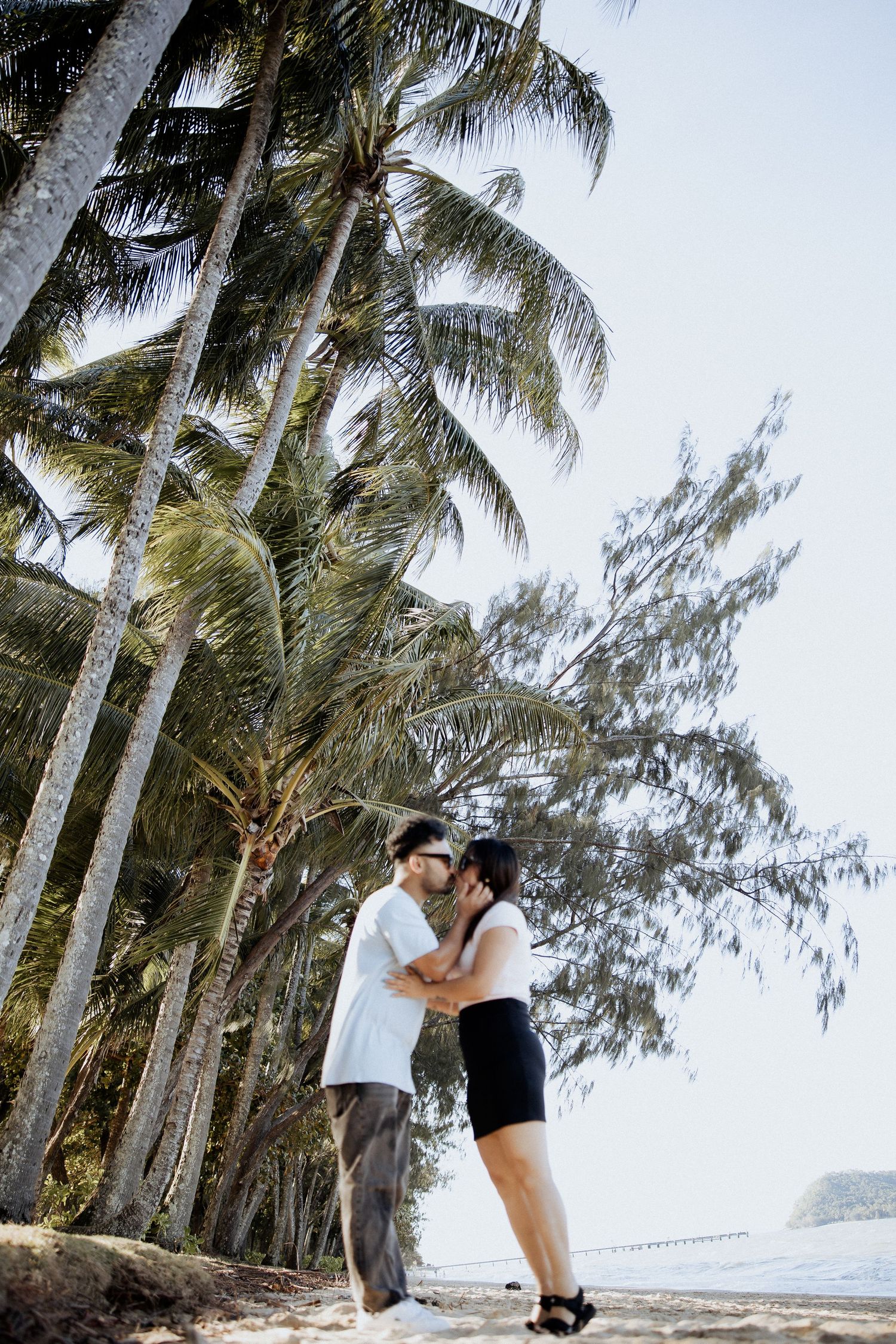 Couple embracing on a palm-lined tropical beach during a sunny day.