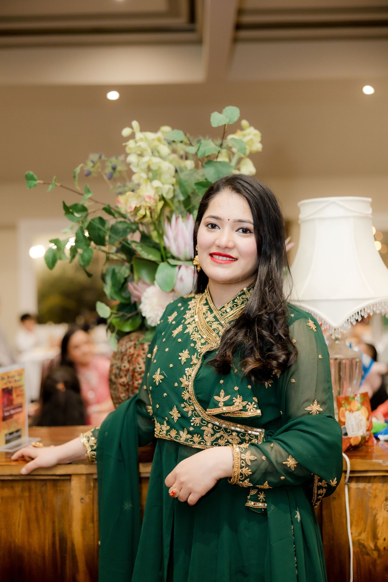 Person in an elegant emerald green dress with gold embroidery poses at an indoor event.