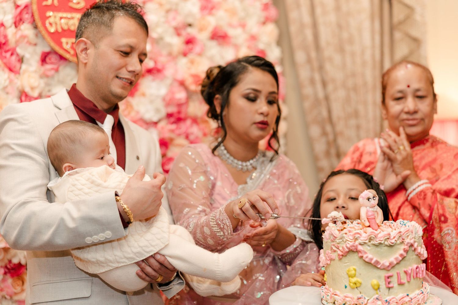 A special family moment during cake celebration with pink floral wall background.