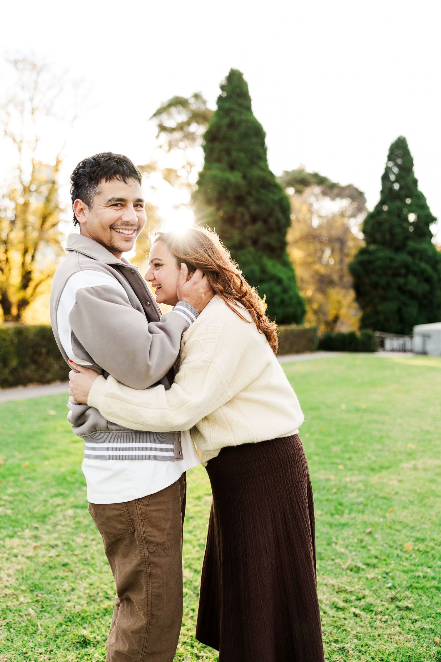 Couple embracing and laughing in a sunny park during autumn.