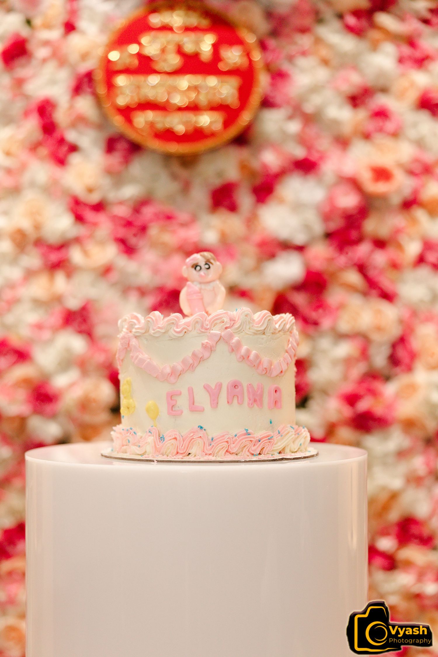 Pink birthday cake with delicate decorations against a floral backdrop.