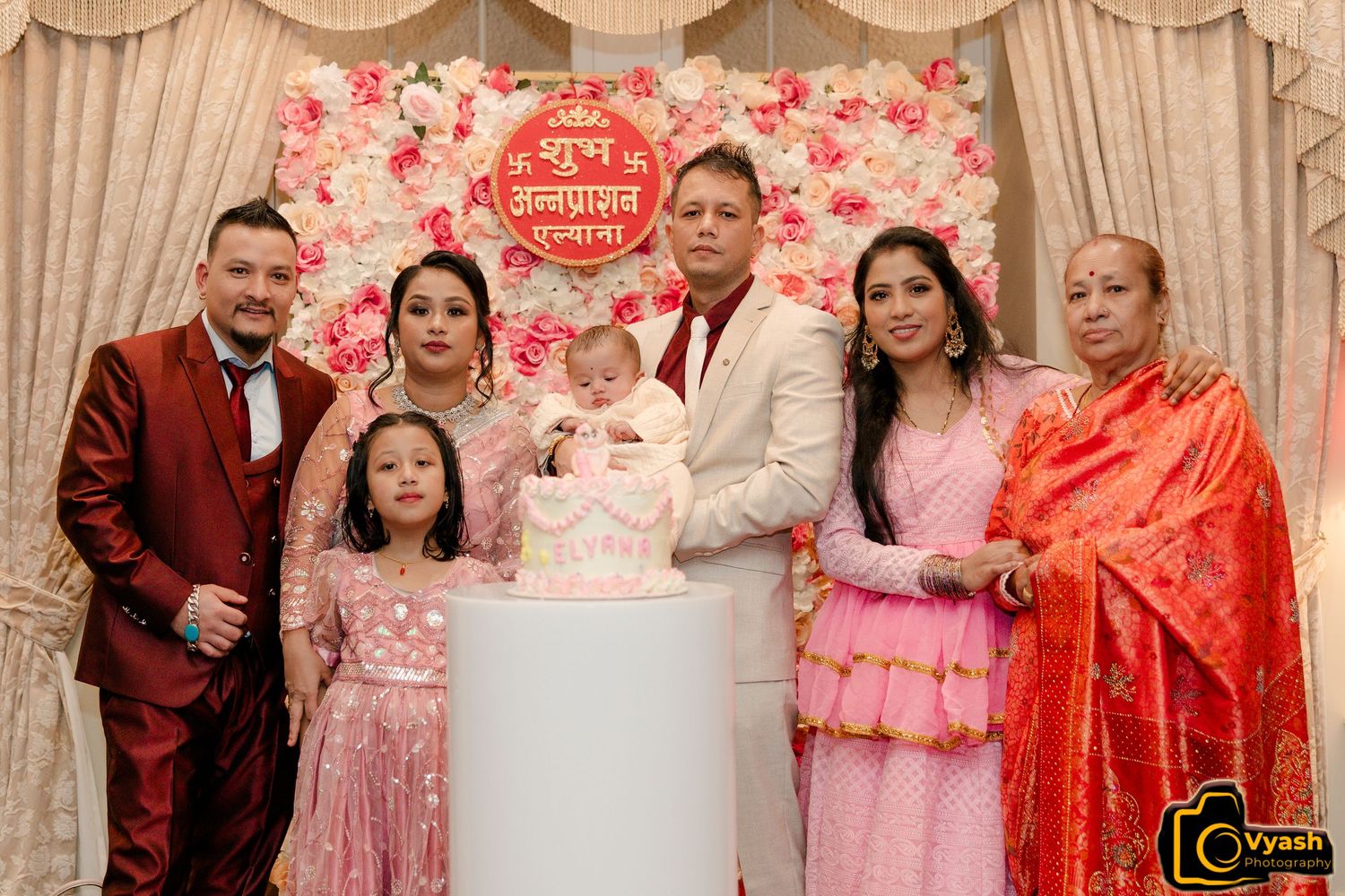 Family celebration with pink cake and floral wall decoration.