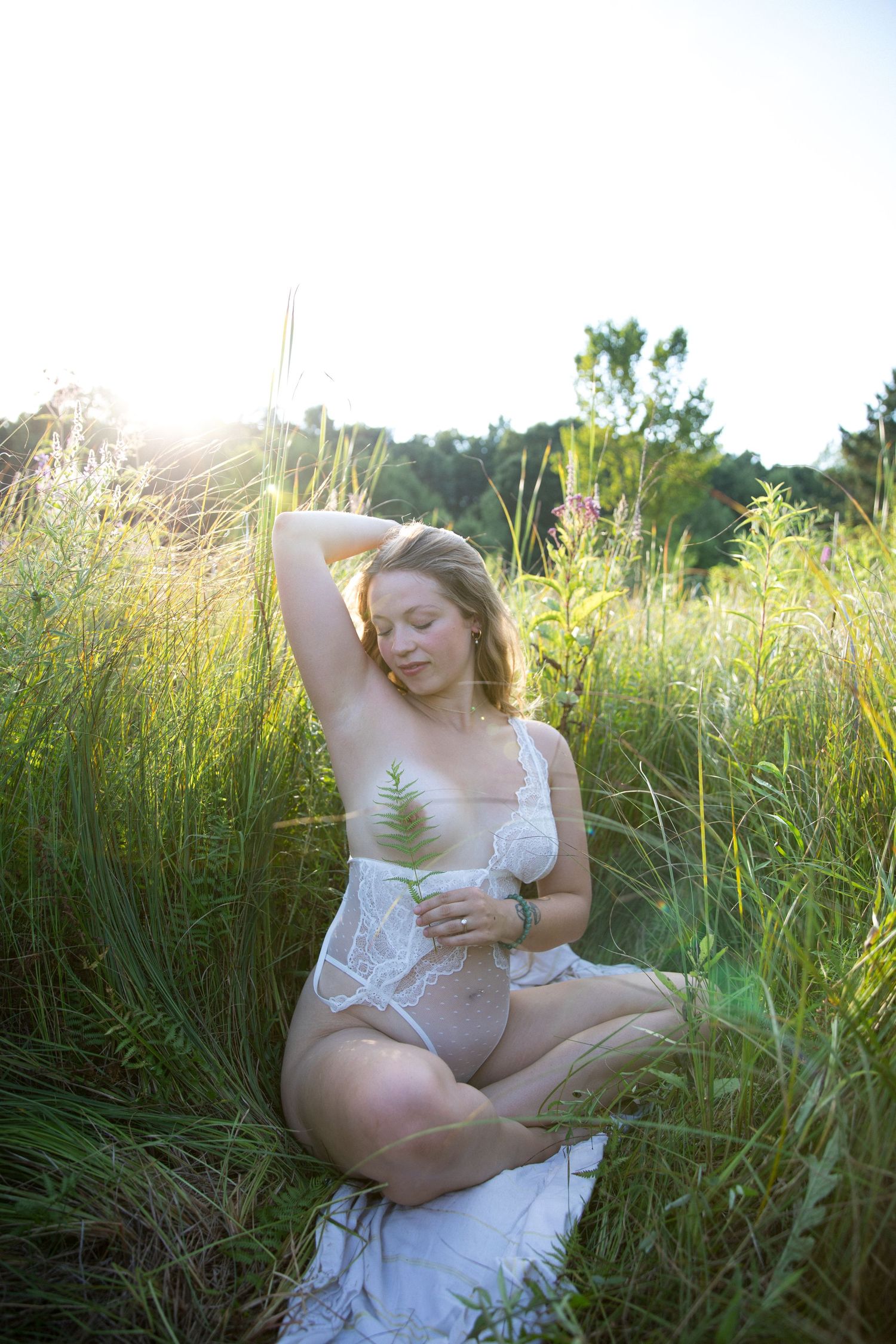 A person in a white dress poses gracefully among tall grasses in golden sunlight during a summer photoshoot.