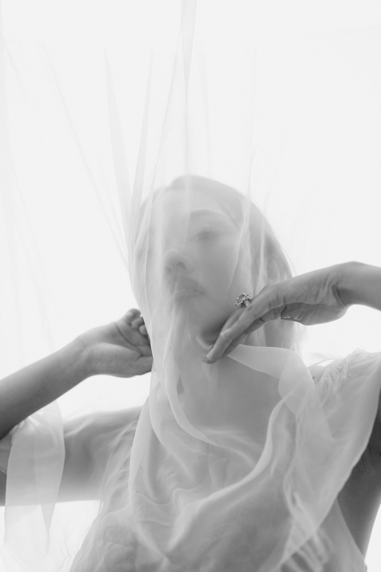 Ethereal black and white portrait through sheer white fabric creating a dreamy, mysterious atmosphere.