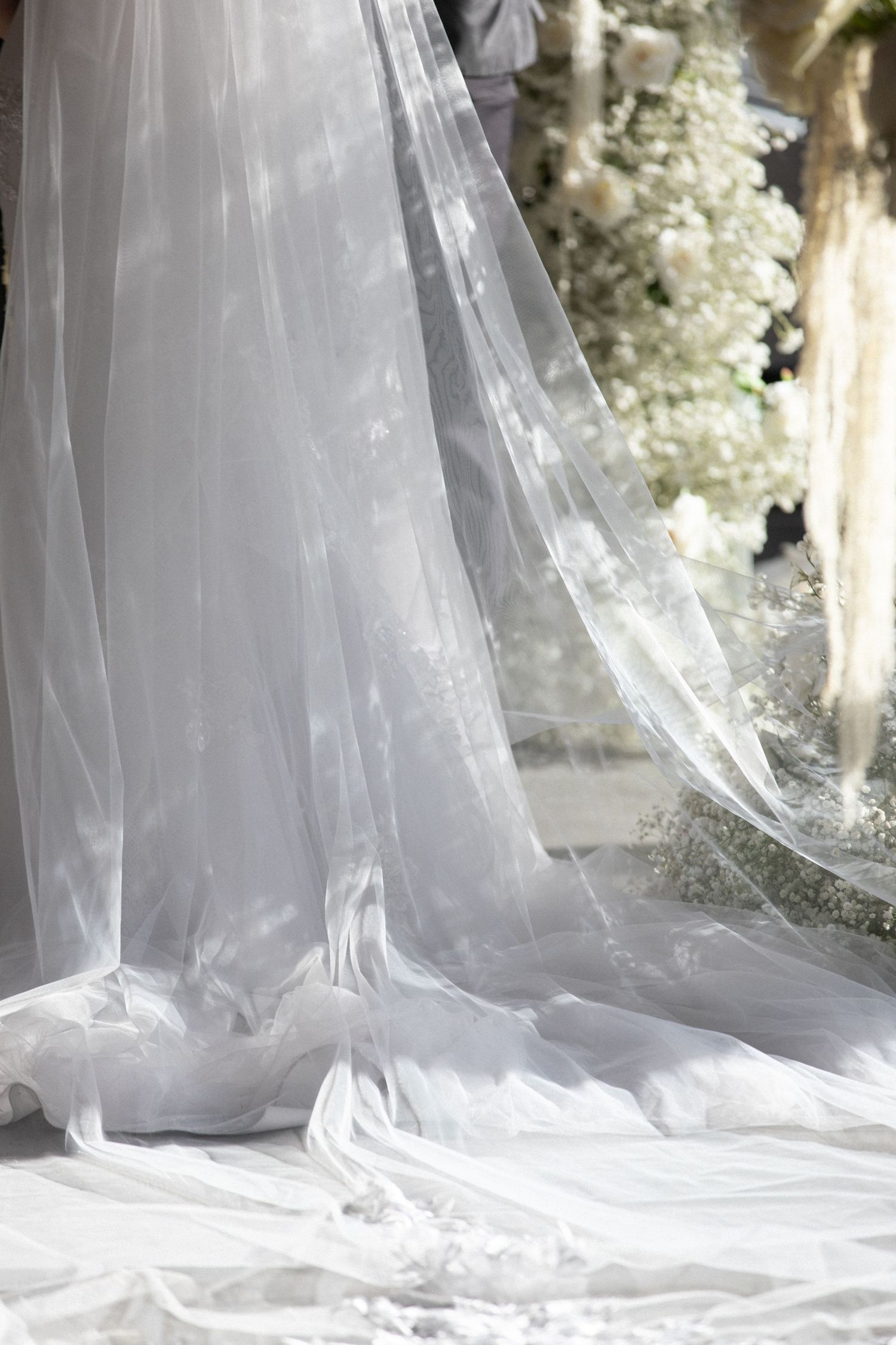 Flowing white bridal gown with sheer veil train draped elegantly on floor at wedding ceremony.