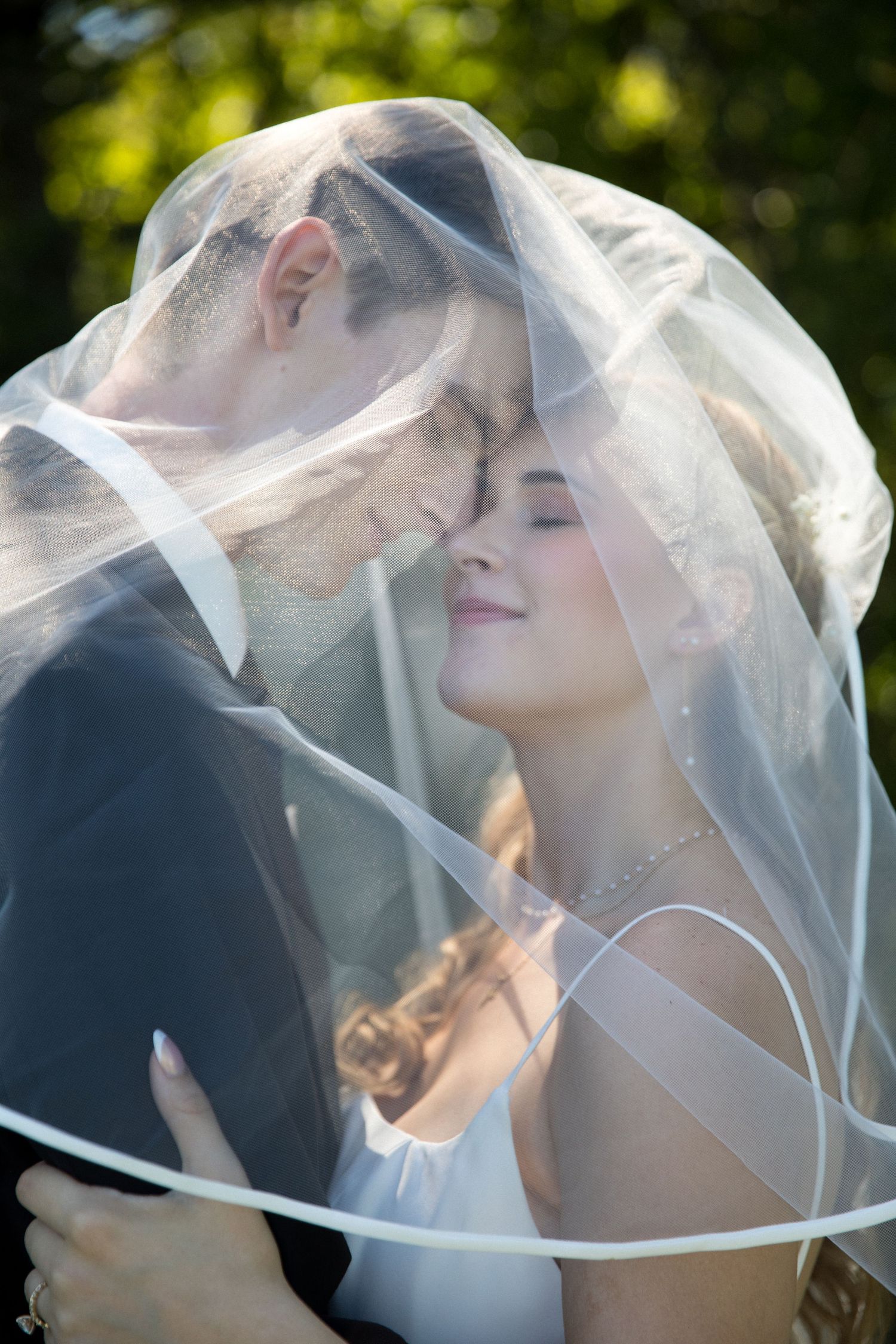 A romantic wedding portrait series showing a couple sharing tender moments under a flowing white veil in natural lighting.