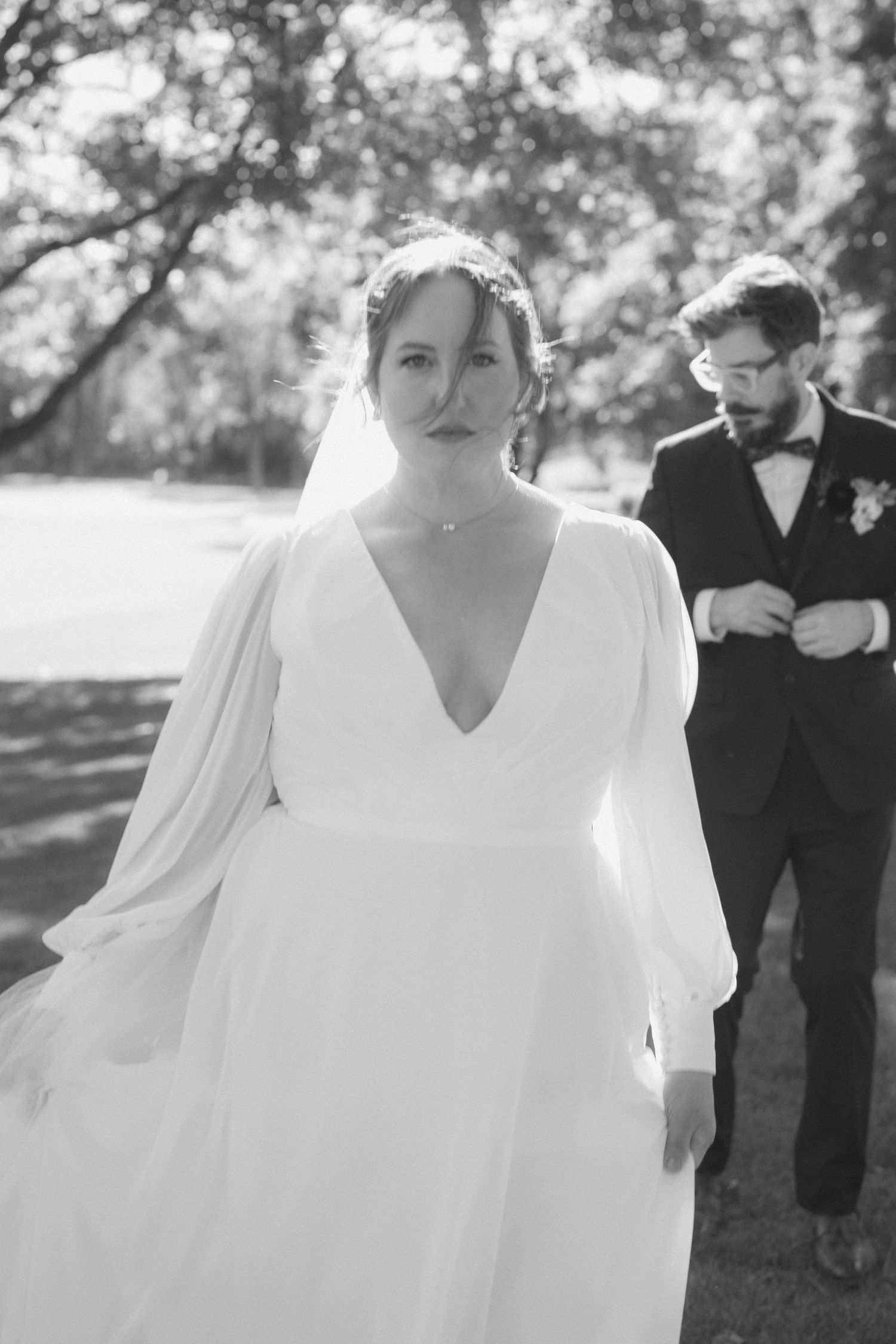Black and white wedding photos show bride in flowing white dress with long sleeves posing outdoors in natural setting.