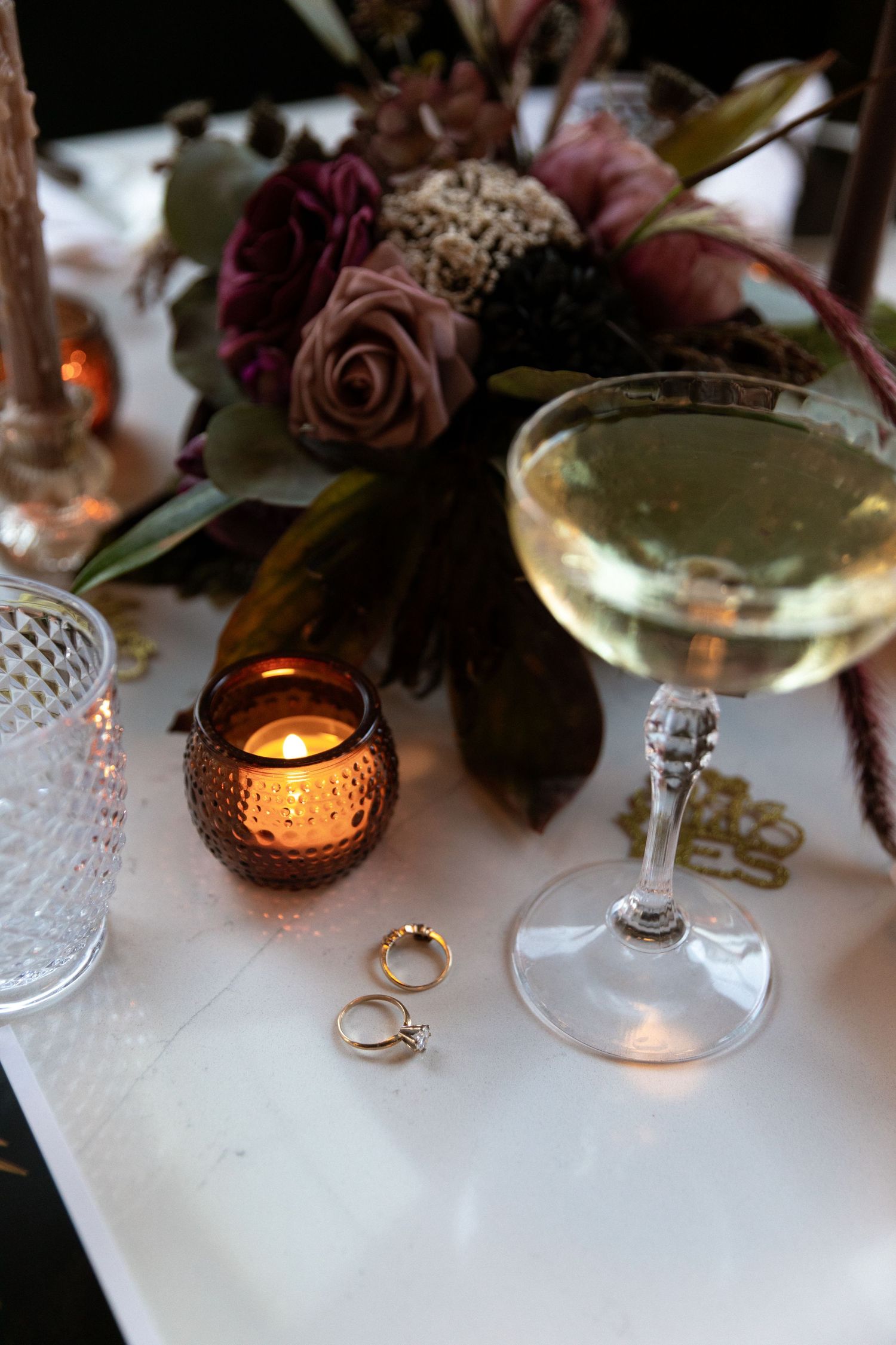 Romantic table setting with dried roses, candlelight, wine glasses and engagement rings creating an intimate ambiance.