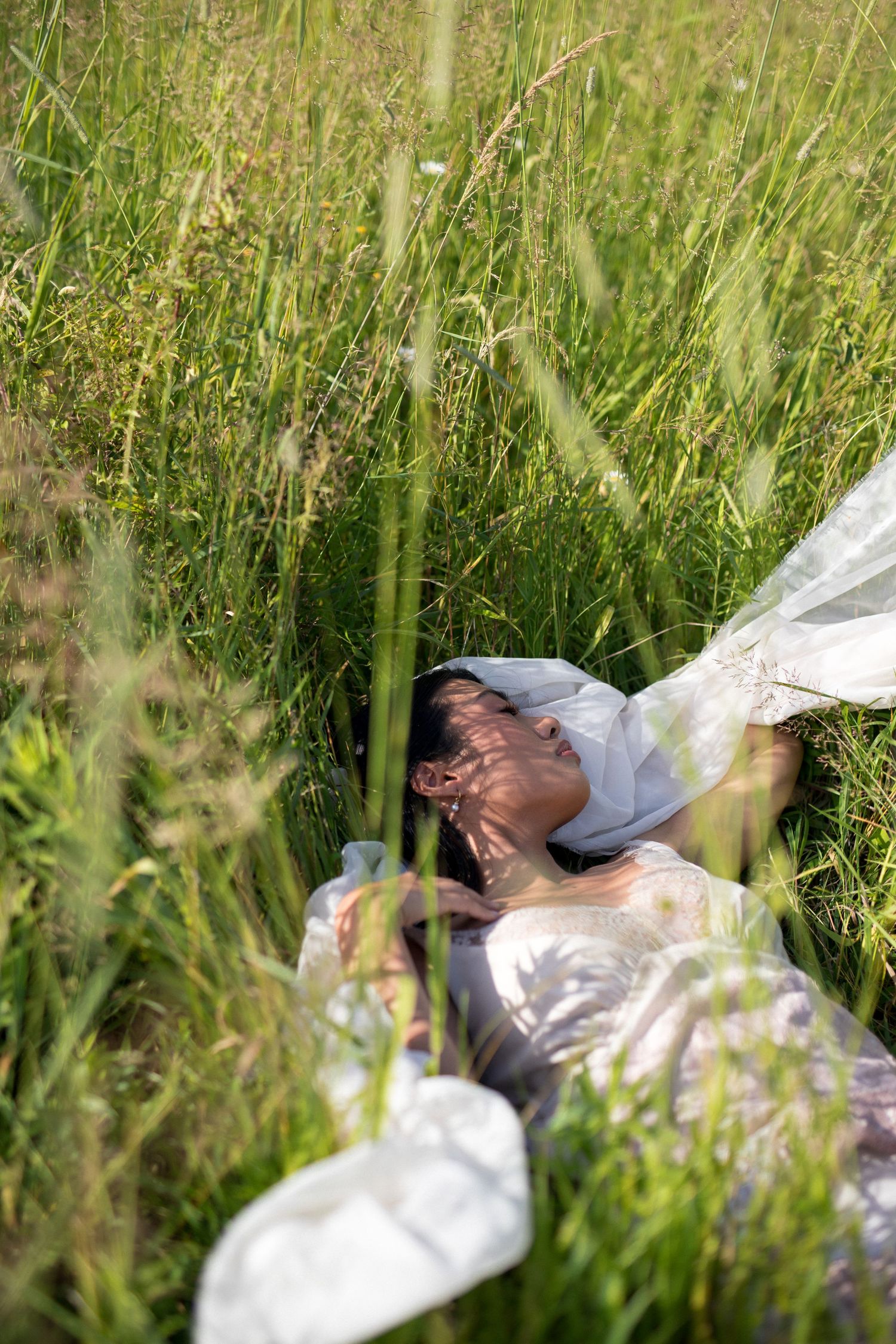 A person lying peacefully in tall grass wearing a white dress, creating a dreamy outdoor portrait scene.