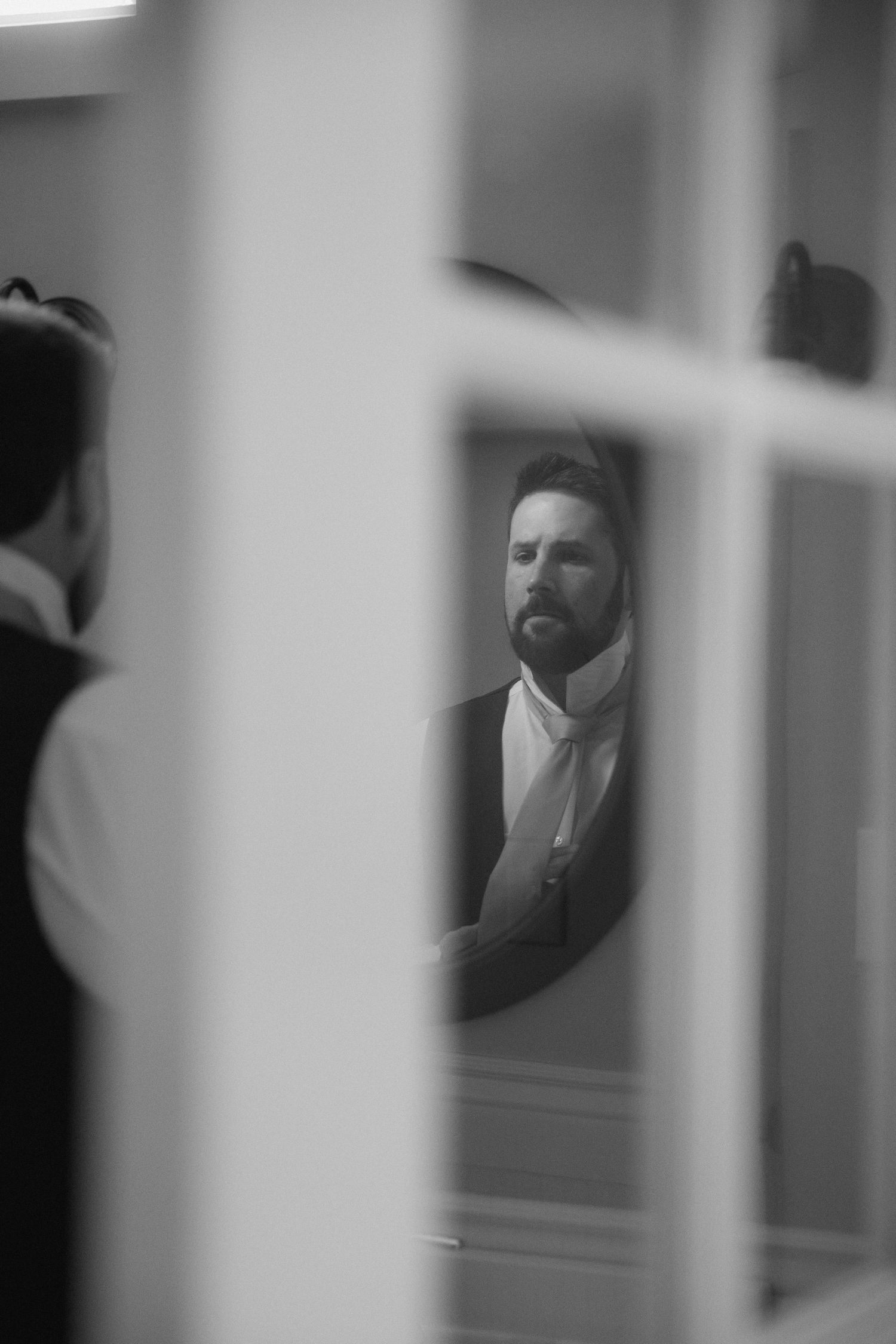 A black and white reflection of a formally dressed person in a window pane, creating a moody artistic composition.