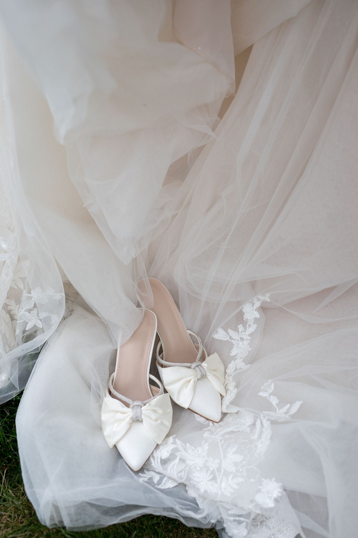 White satin bridal shoes peek out from beneath layers of delicate tulle wedding dress fabric.