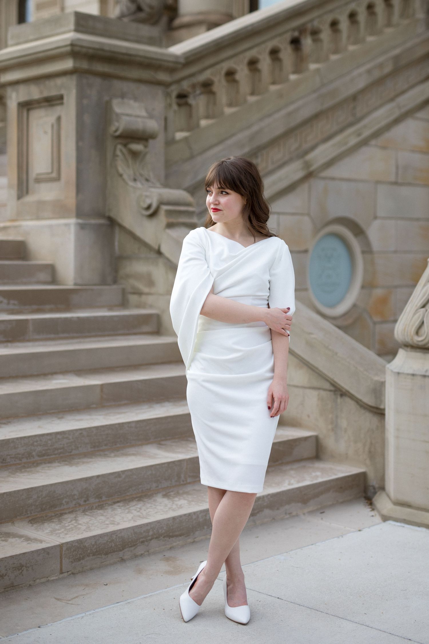 A person in a chic white mini dress and heels poses elegantly on ornate stone steps in a series of fashion photos.