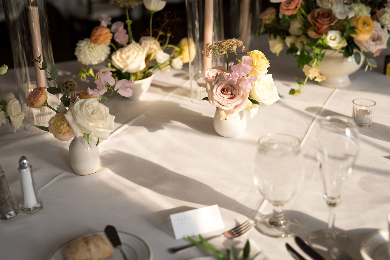 Elegant wedding reception tables decorated with soft pink and white floral centerpieces and glowing candlelight.