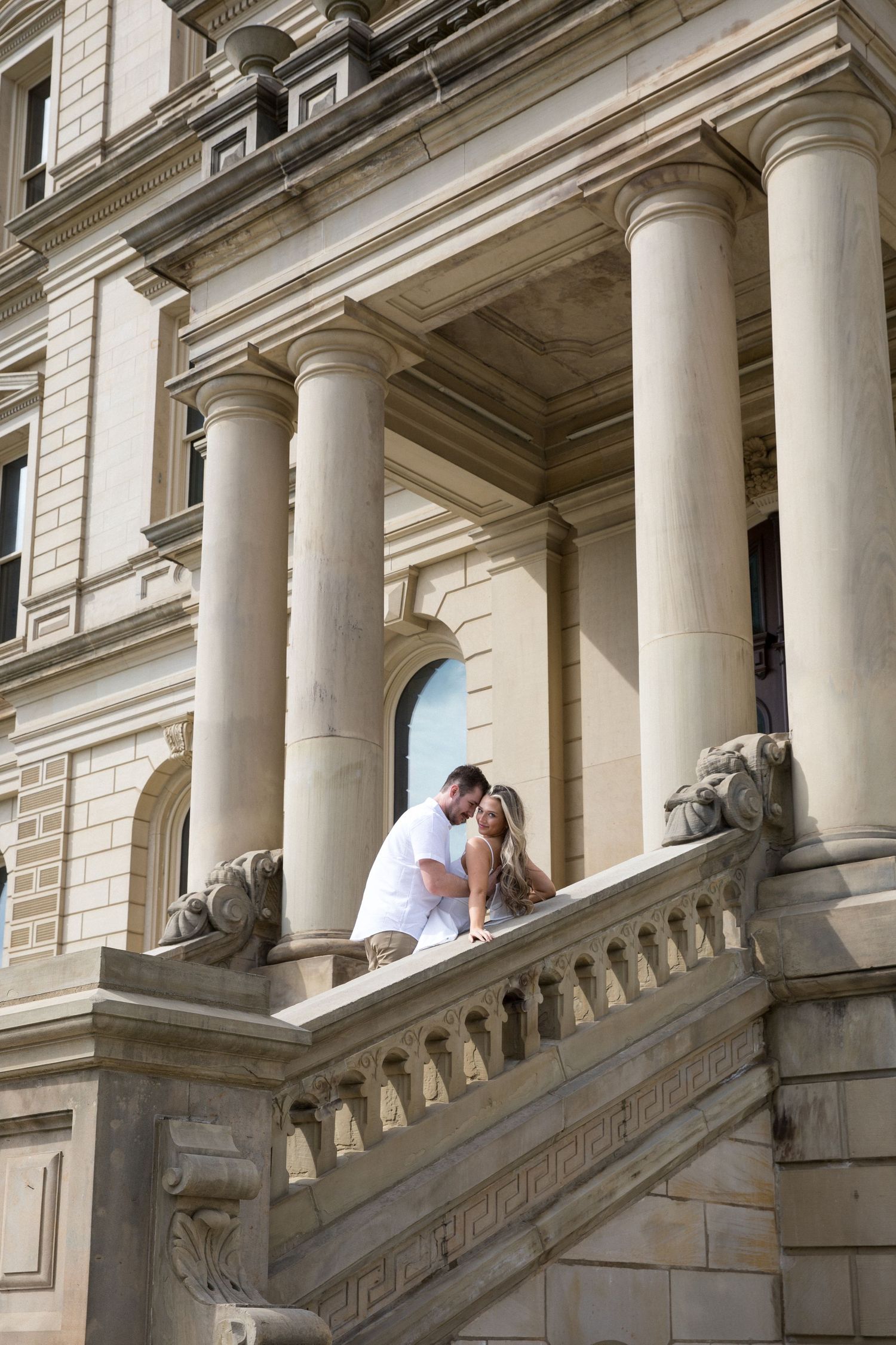 Couple embracing on ornate stone staircase with classical columns of historic building.