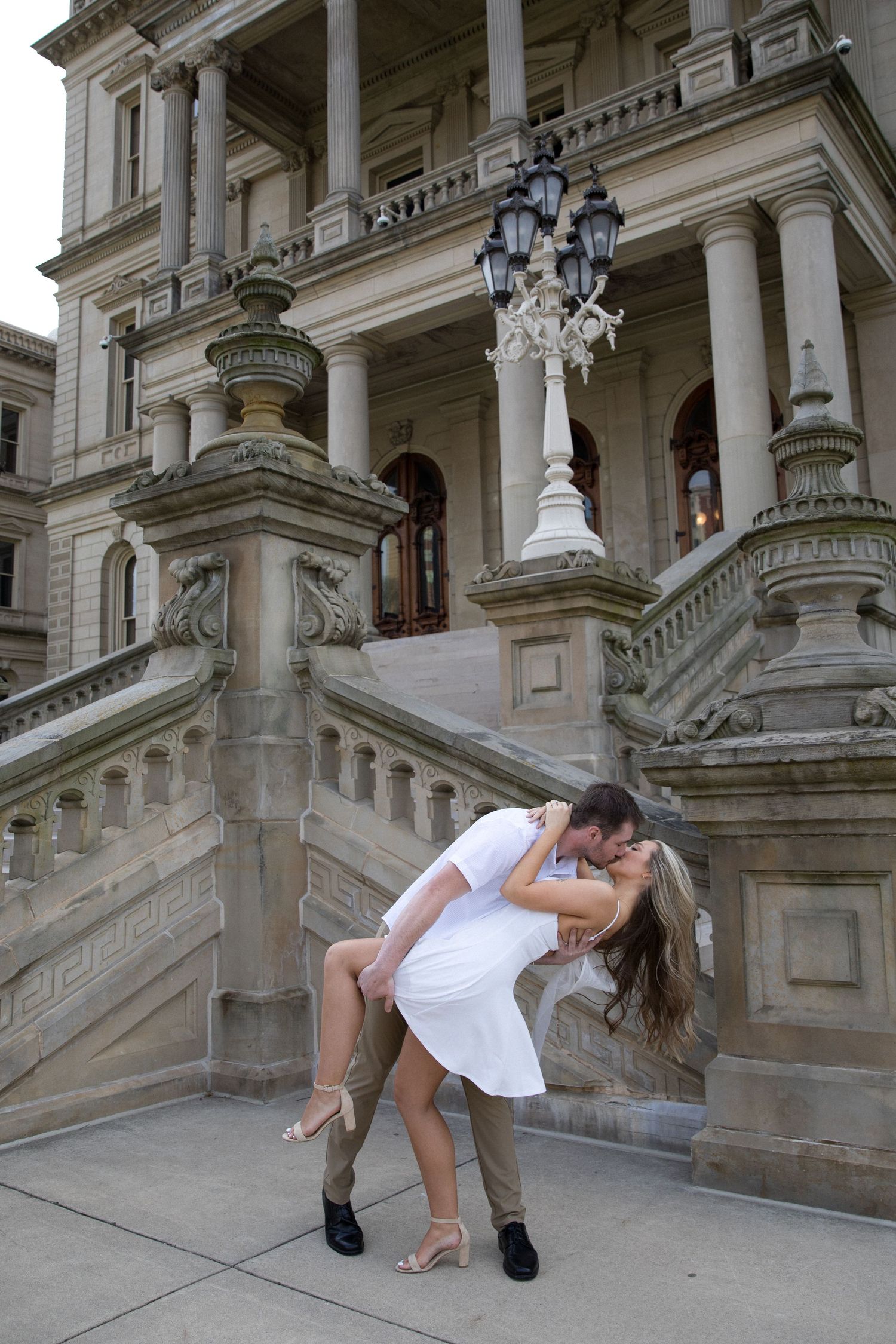 Couple sharing a romantic dip kiss in front of a grand stone building with ornate columns and staircase.