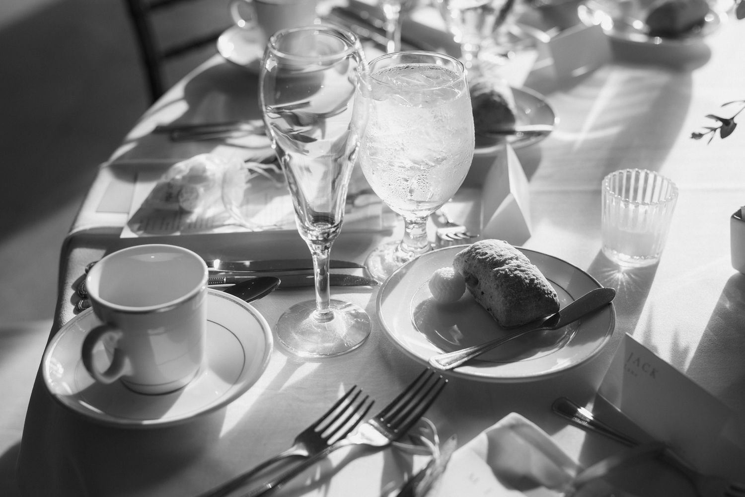 Black and white photo of elegant table settings with wine glasses and plates at a formal dining event.