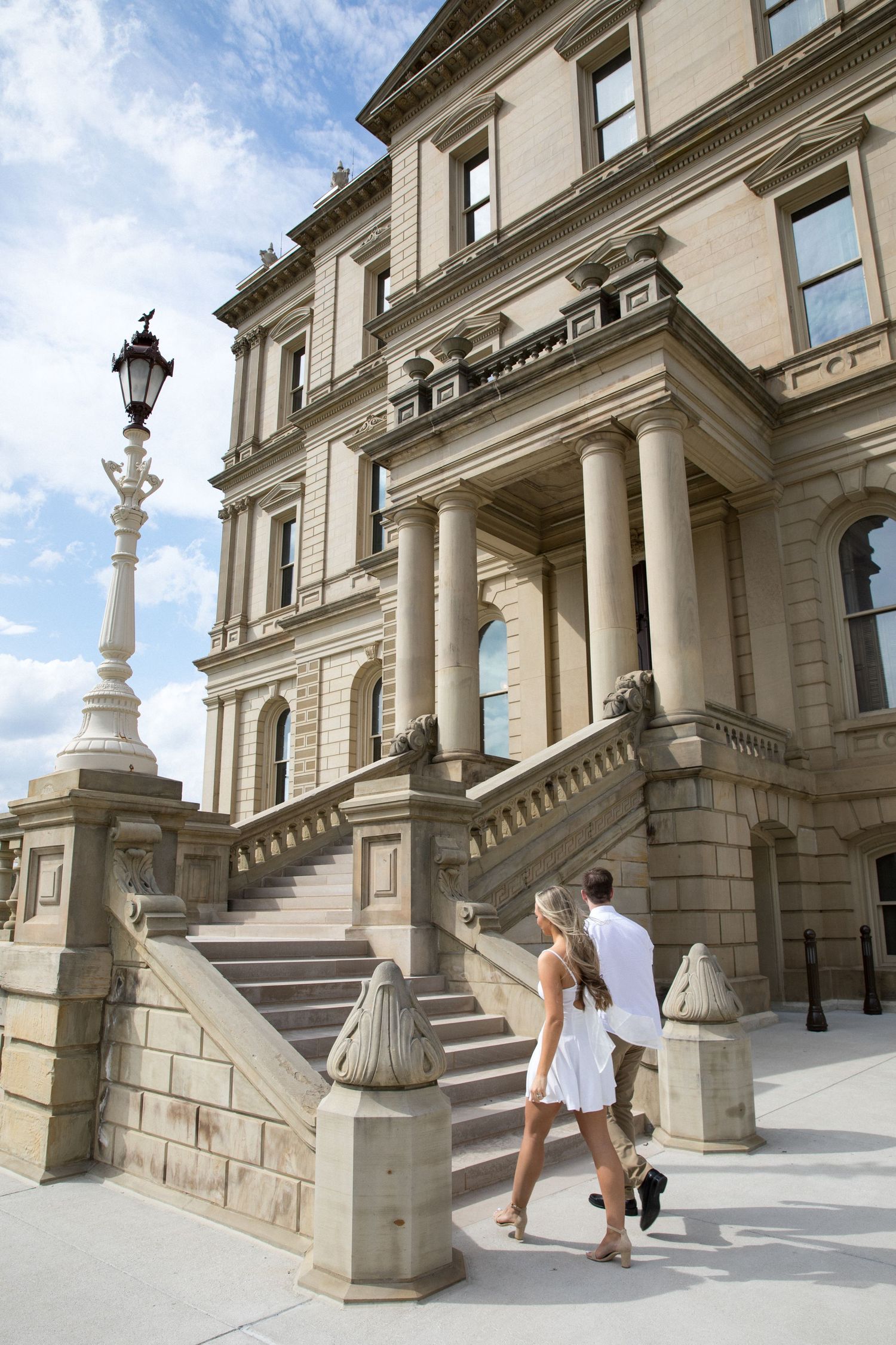 Couple walking up steps of a grand neoclassical government building with columns and ornate lamp post.