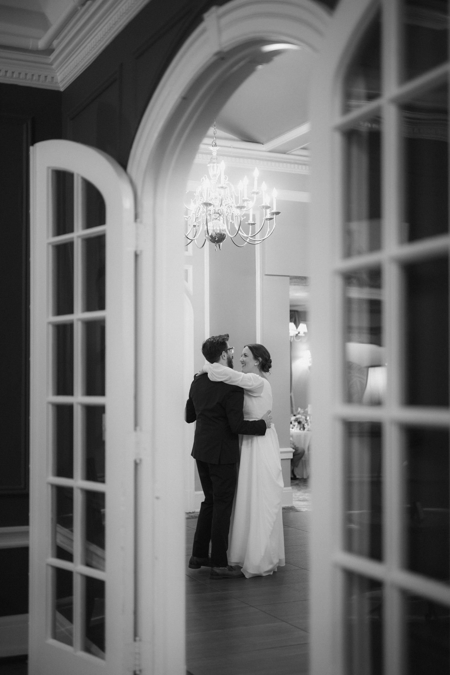 A romantic black and white wedding dance sequence showing a couple in an elegant hallway with chandeliers.