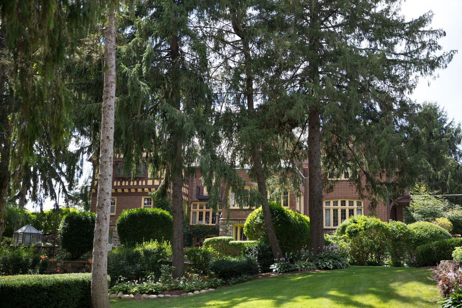 Tall evergreen trees line a landscaped garden path with lush green grass and decorative fencing.