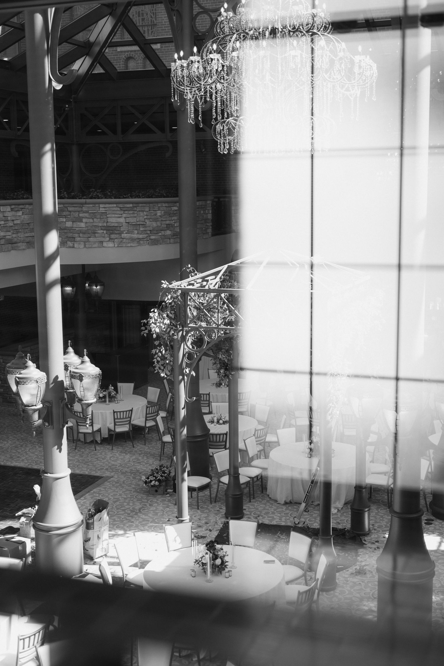 Crystal chandeliers hang in an elegant venue space with brick walls and sheer curtains creating a romantic ambiance.