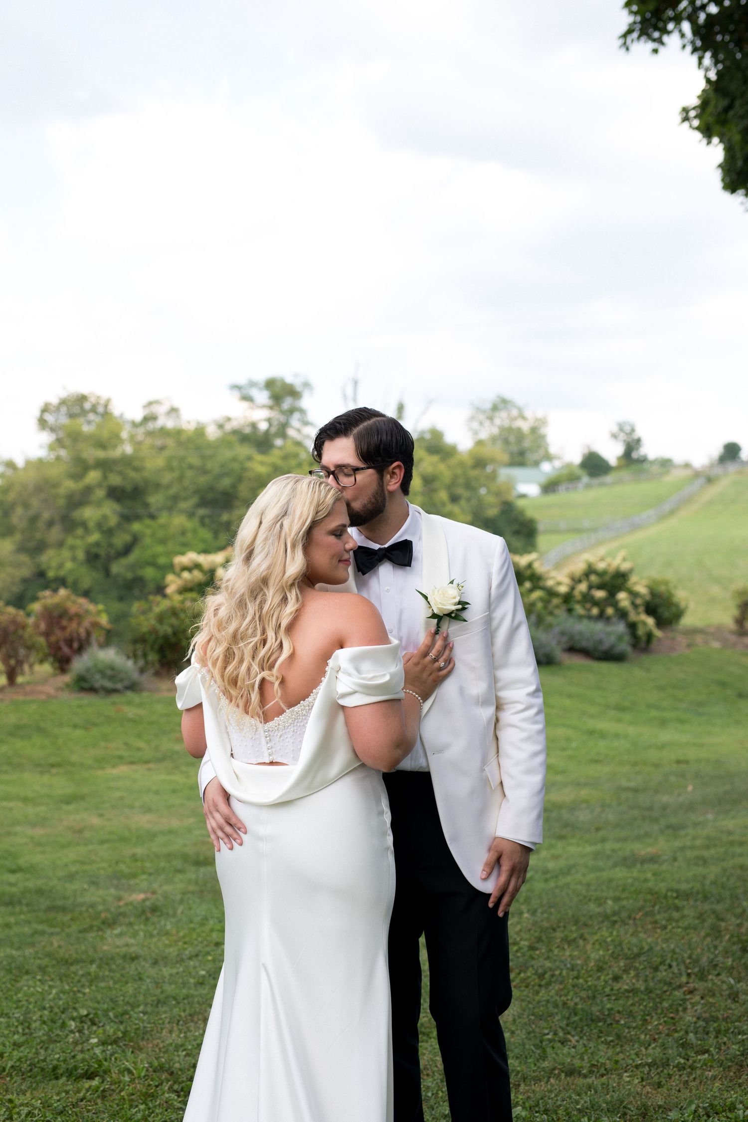 A couple shares a romantic moment on their wedding day in an elegant outdoor setting with rolling hills in the background.