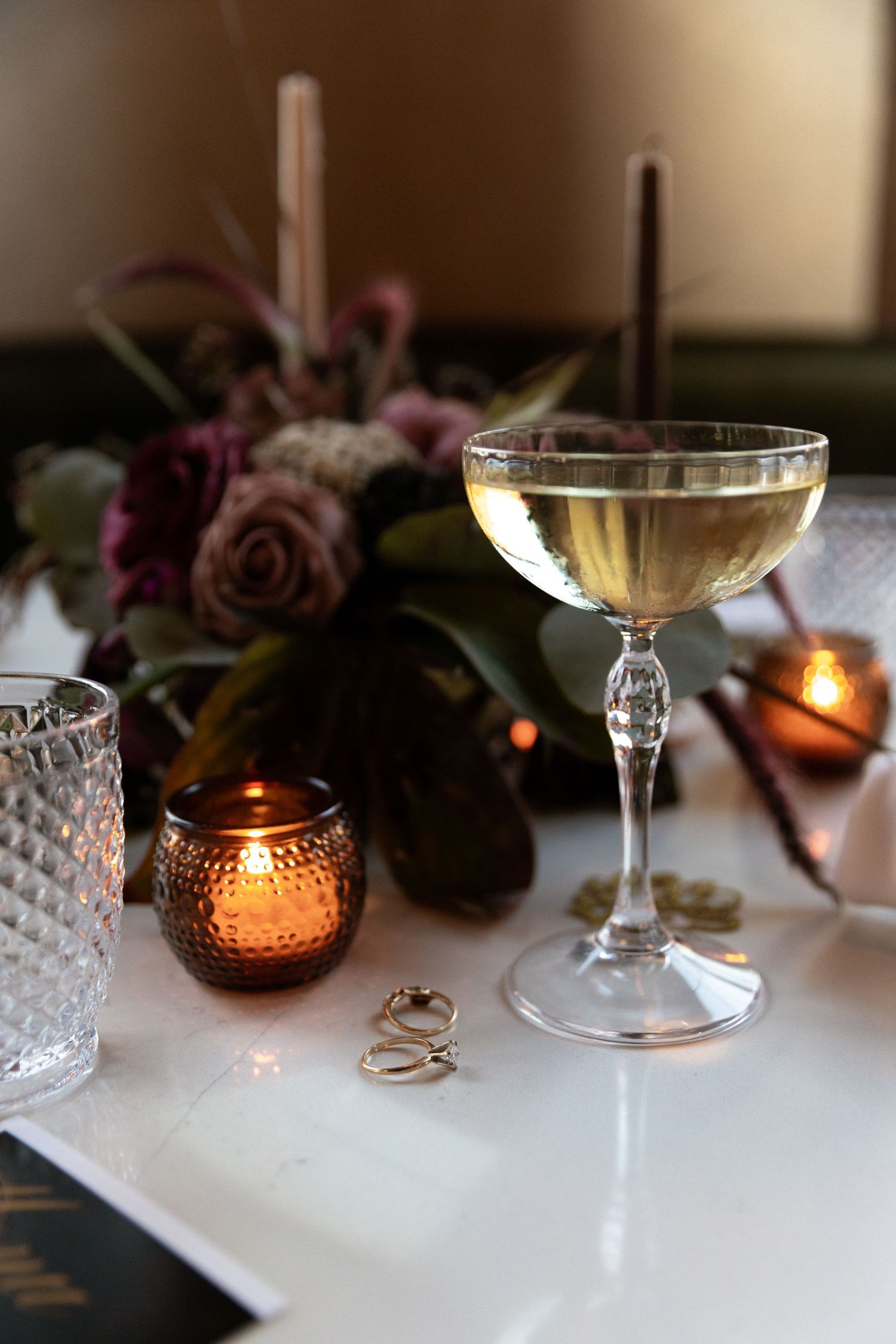 Elegant wine glasses and glowing candles create a romantic table setting with soft lighting and pink roses.
