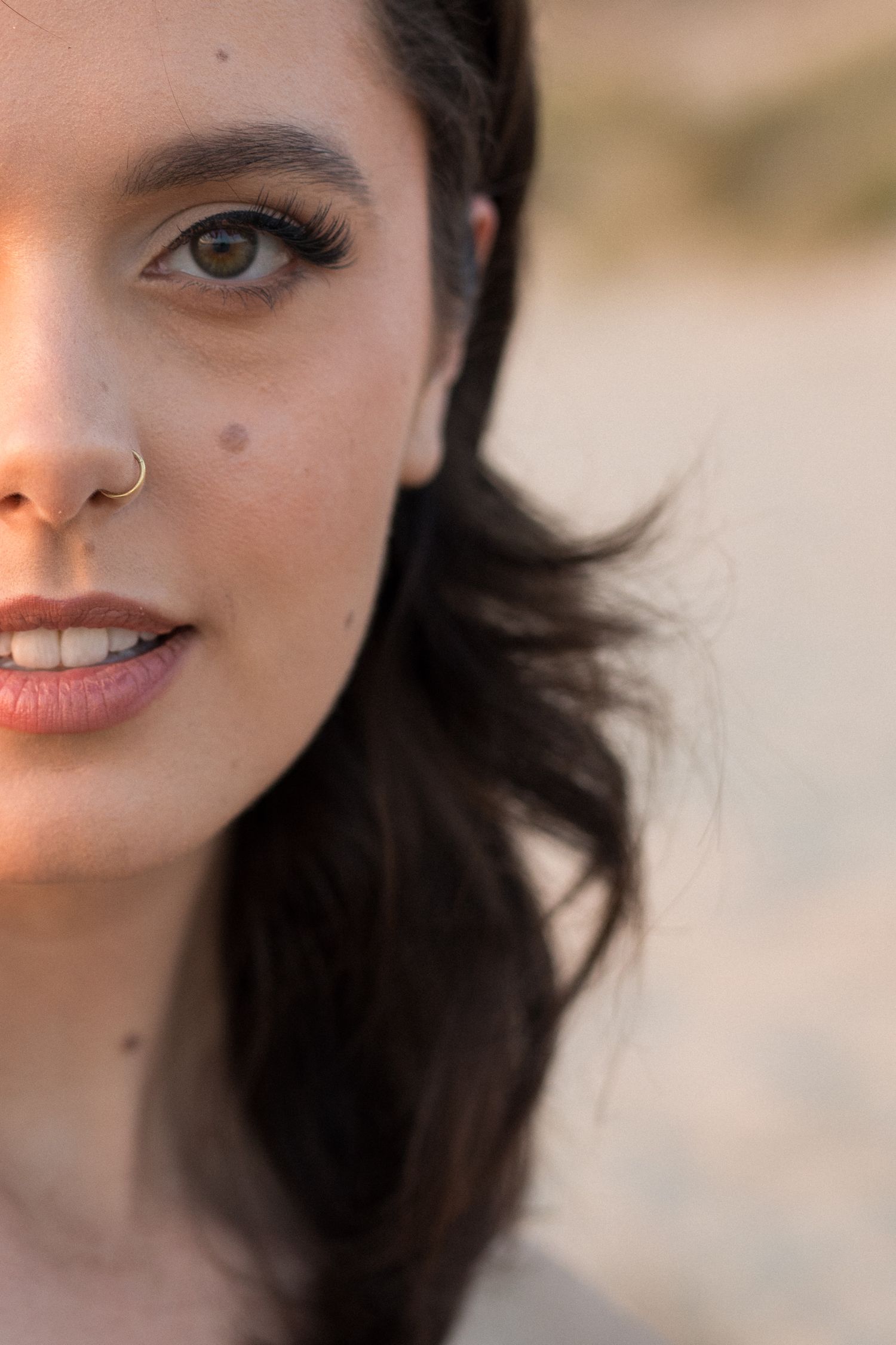 Close up portrait with dark hair and nose piercing in warm natural lighting.